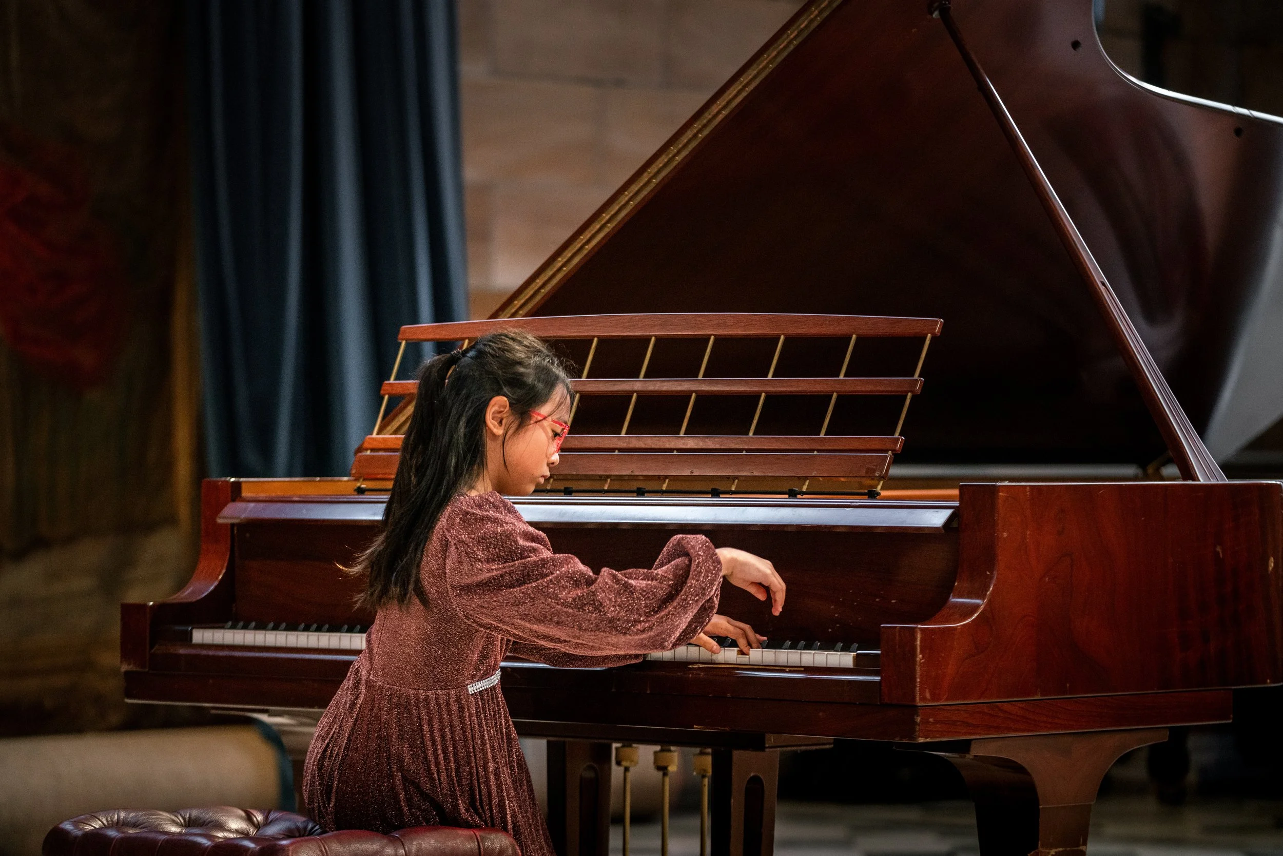 Young girl playing grand piano on stage during a performance.