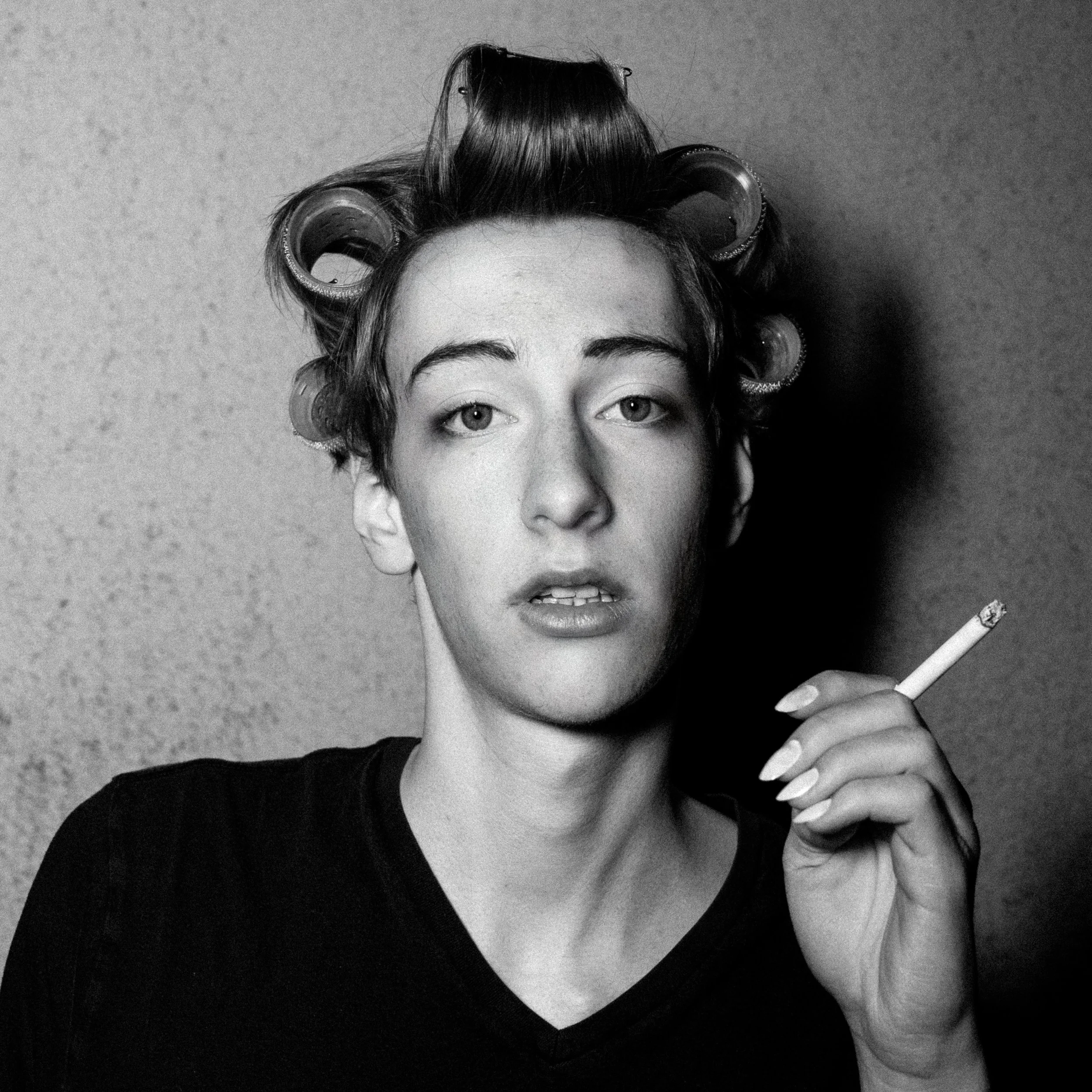 Schwarz-Weiß-Foto einer Frau mit Haarrollen im Haar, die einen Zigarettenzug hält.