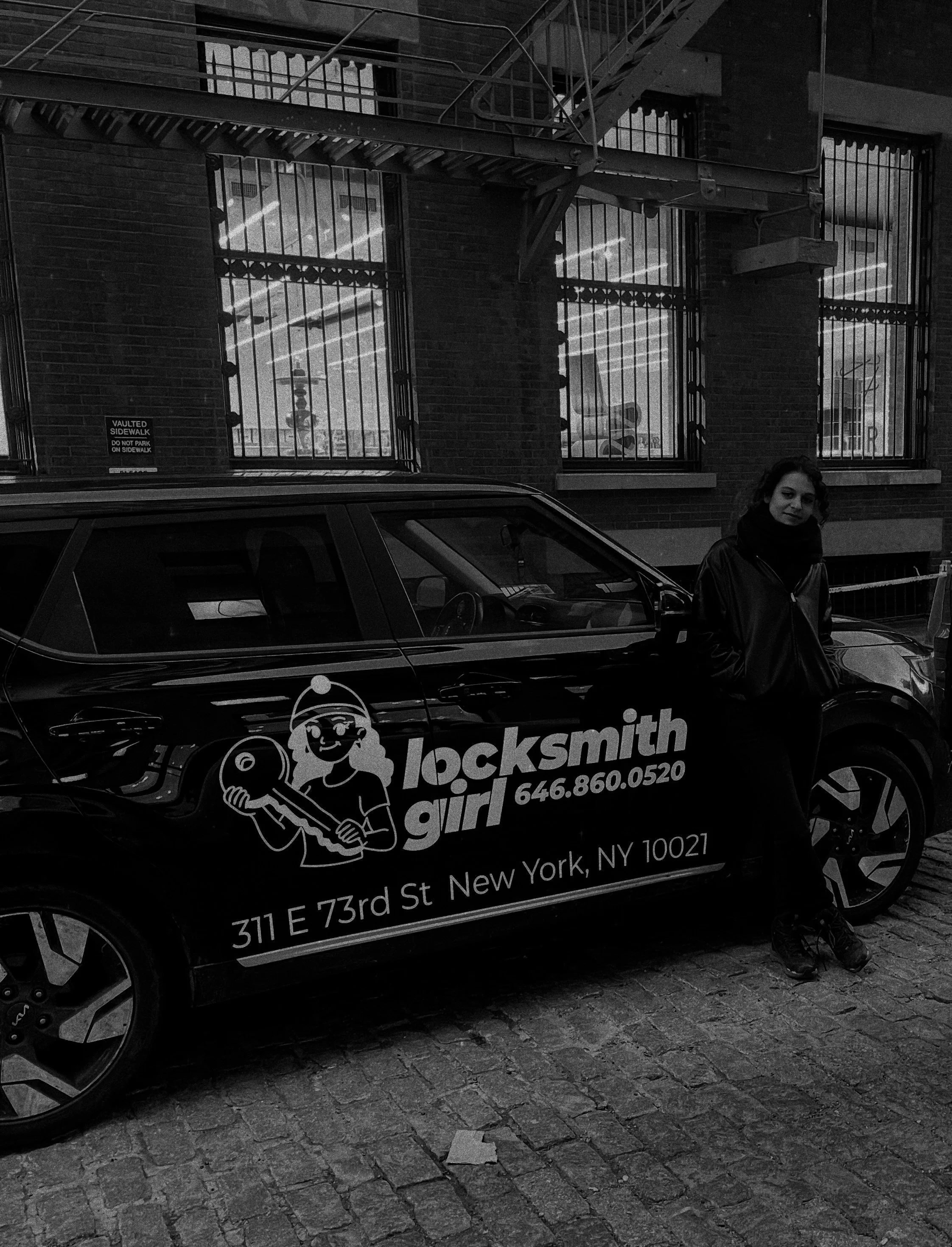 A woman leaning against a black locksmith car on a city street. The car has a logo of a girl holding a key, with text reading "locksmith girl", a phone number, and an address in New York.