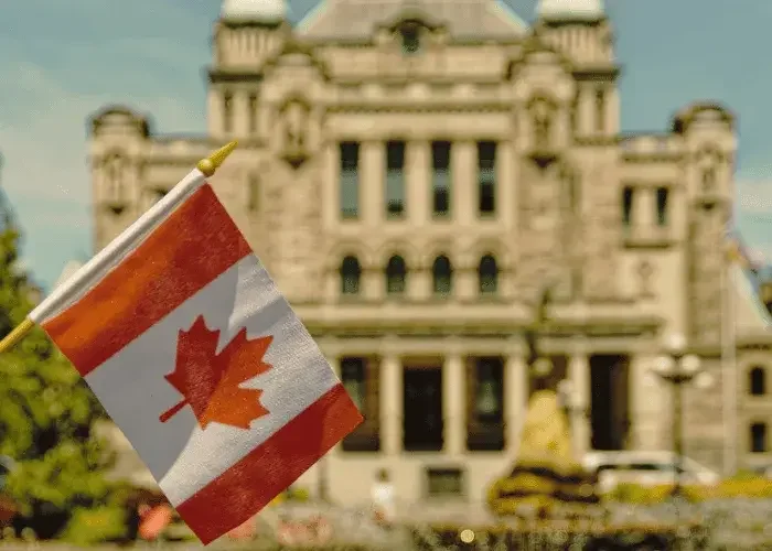 Drapeau du Canada devant un ancien bâtiment en pierre, avec un ciel bleu en arrière-plan.