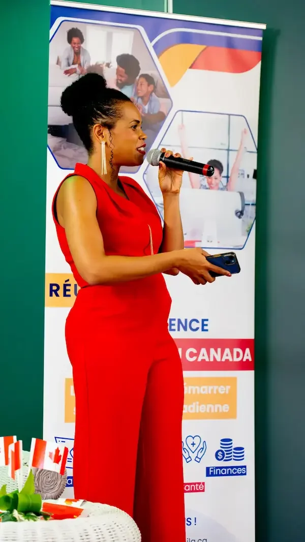 Sandrine Edmond  Une femme en robe rouge parle dans un microphone devant une bannière promotionnelle.