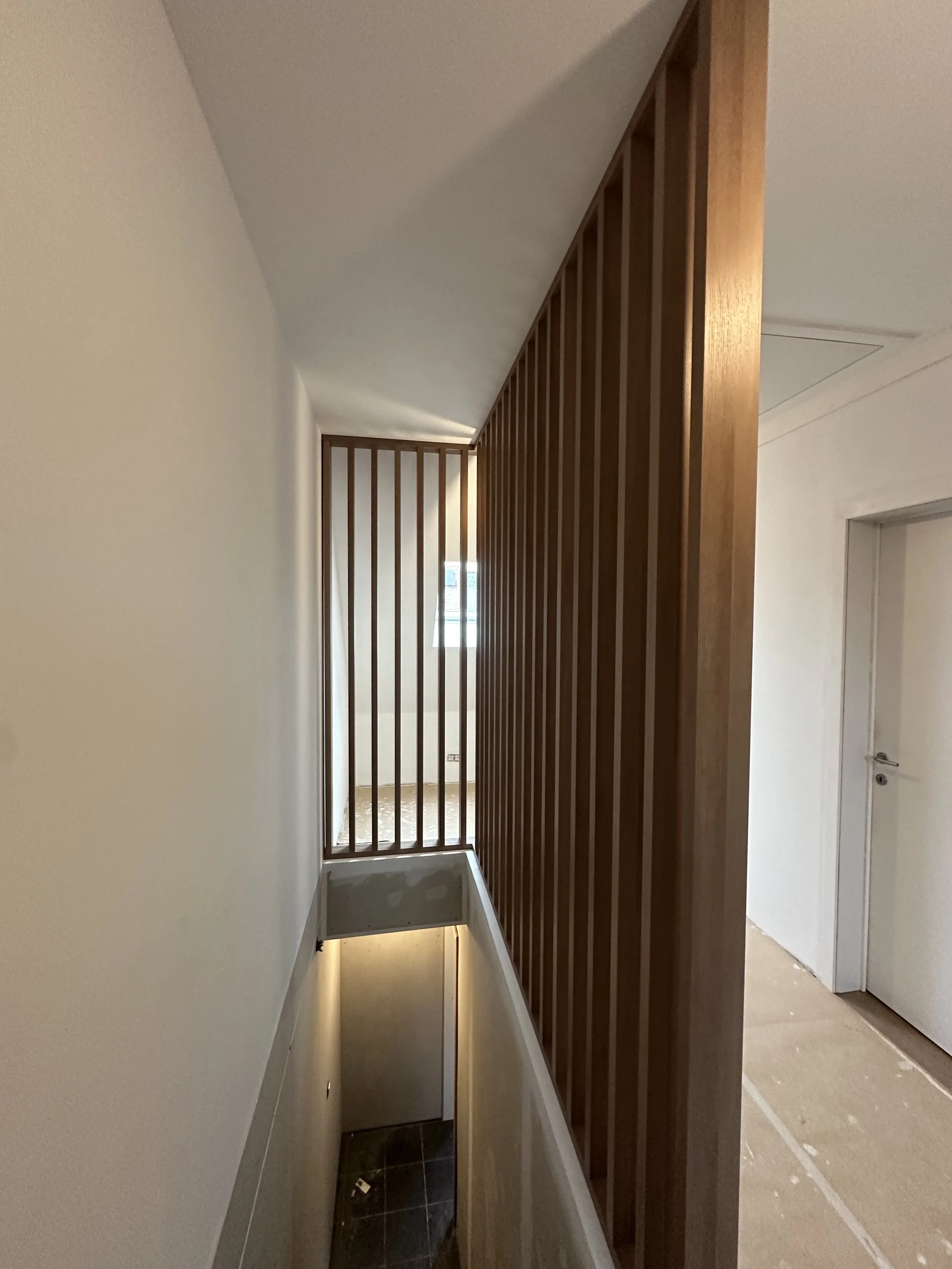 Houten stijlwand met verticale lamellen langs traphal, schrijnwerk op maat door Sorgeloose in Brugge