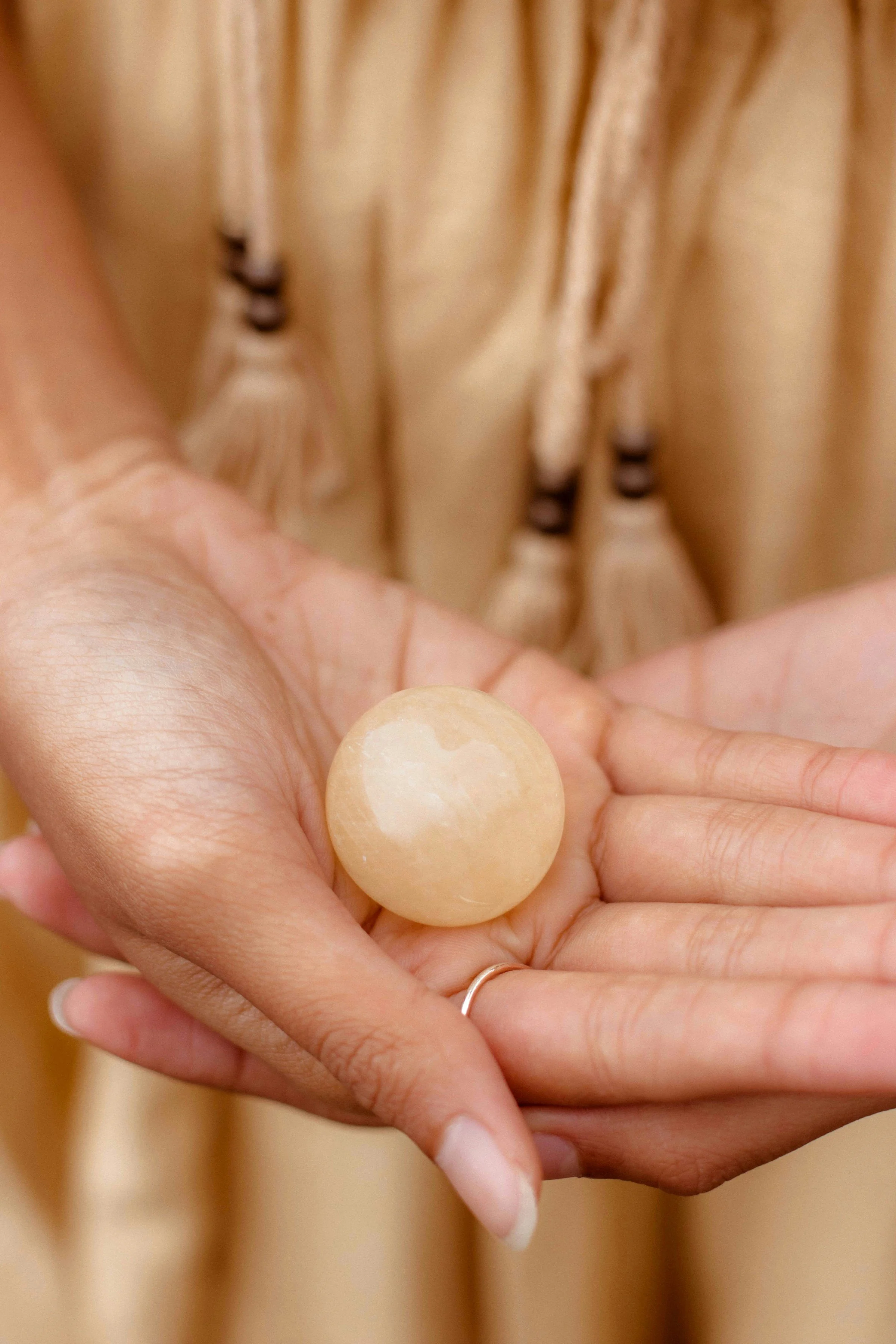 A person holding a round, beige jewelry stone in their palm.