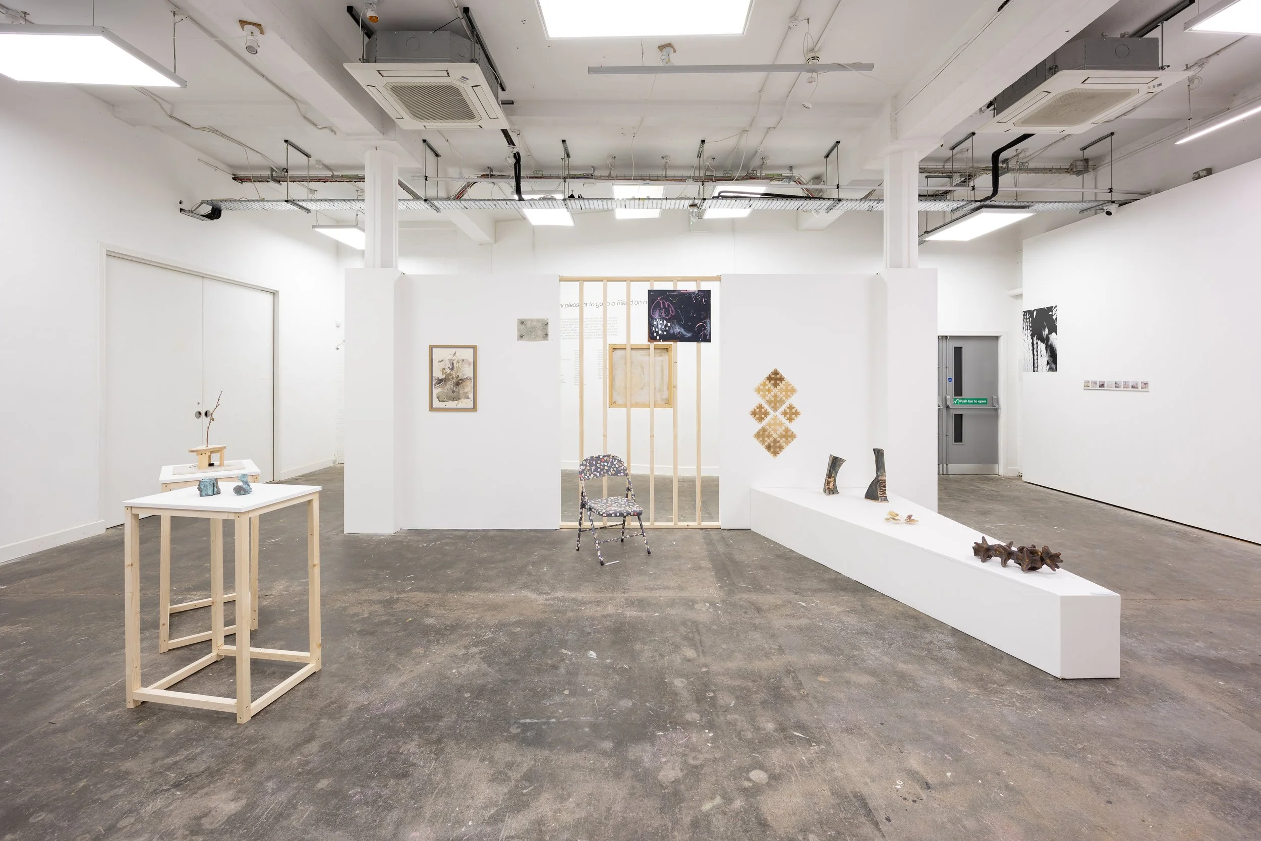 An art gallery with white walls displaying various artworks, including paintings, sculptures, and mixed media pieces, with spotlights illuminating the pieces.