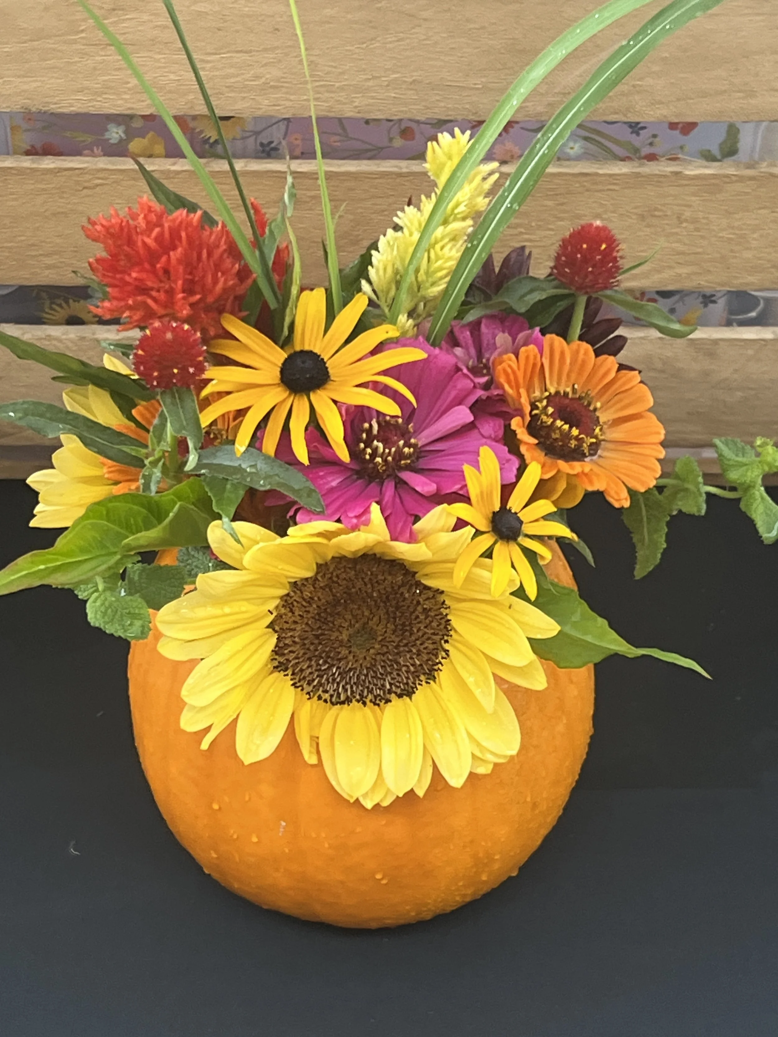 A decorative flower arrangement in a pumpkin, consisting of colorful flowers such as sunflowers, daisies, and other bright blossoms.