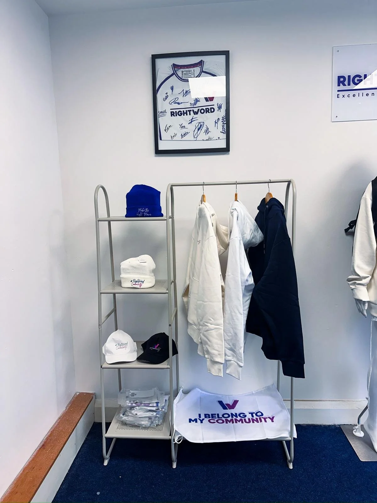 Display of merchandise including hats and jackets related to the community, with a framed signed sports jersey and promotional signs on the wall.