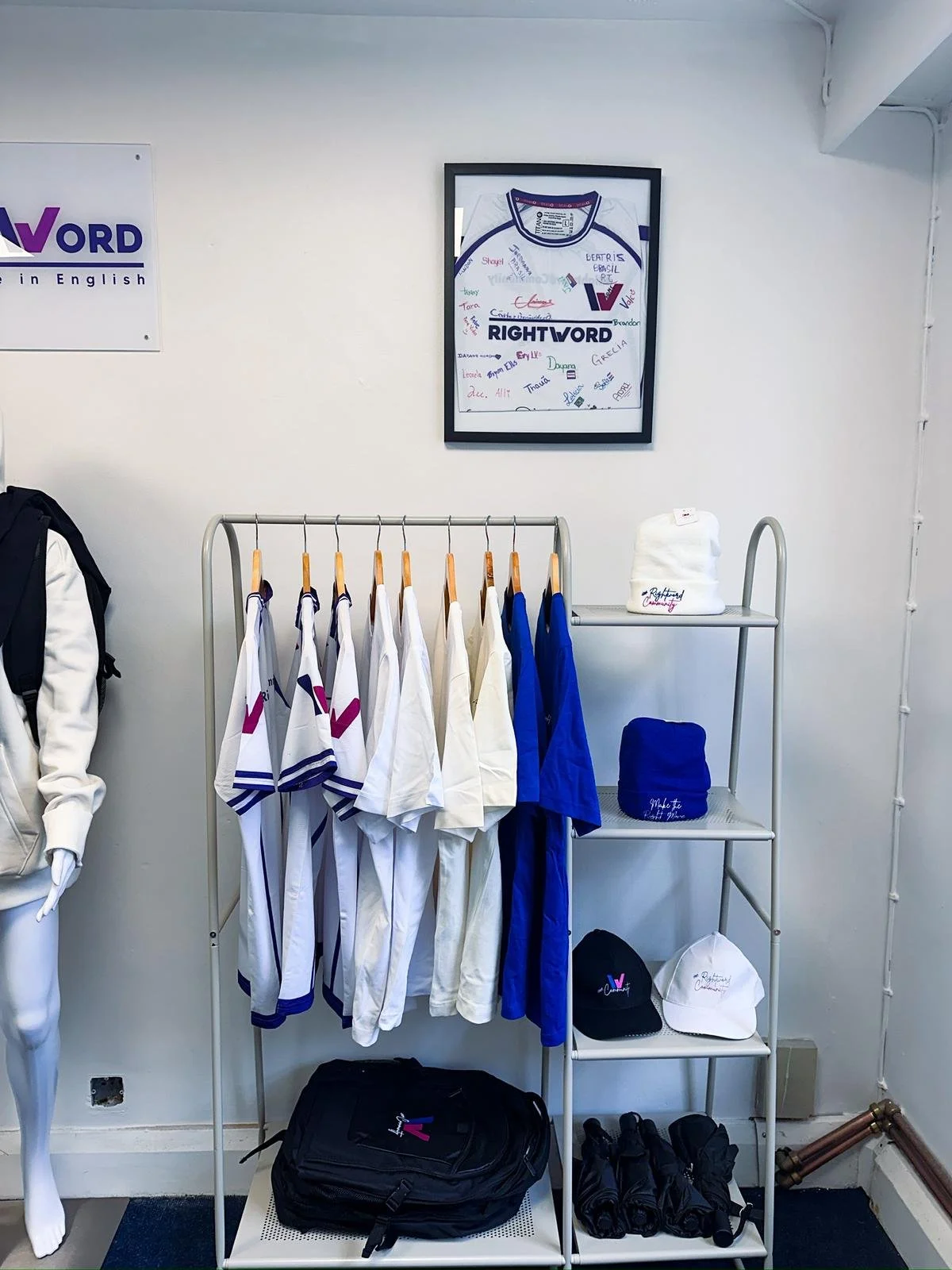 Display of sportswear including jerseys, hats, and bags on shelves and rack, with a framed signed sports jersey on the wall.