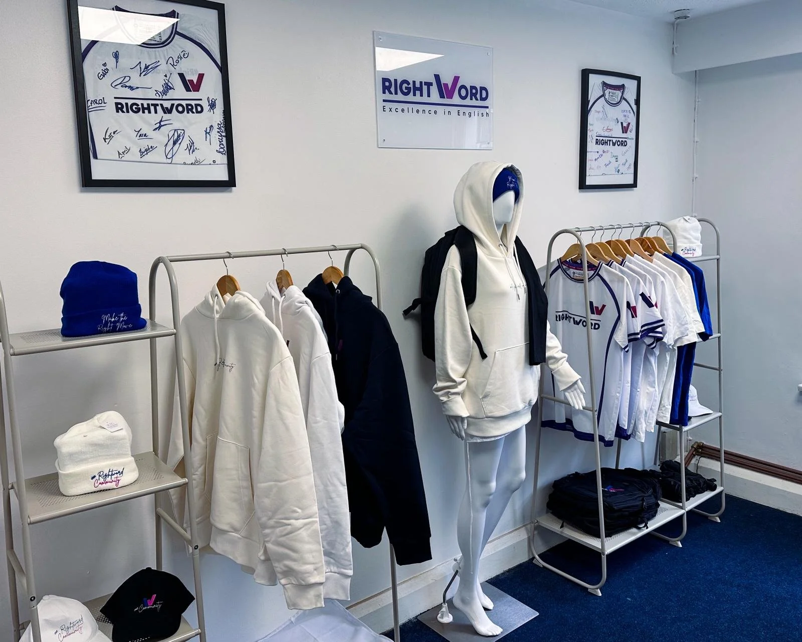 Display of sportswear including hoodies, jackets, jerseys, hats, and backpacks at RIGHT WORD store, with framed signed sports jerseys and a sign on the wall.