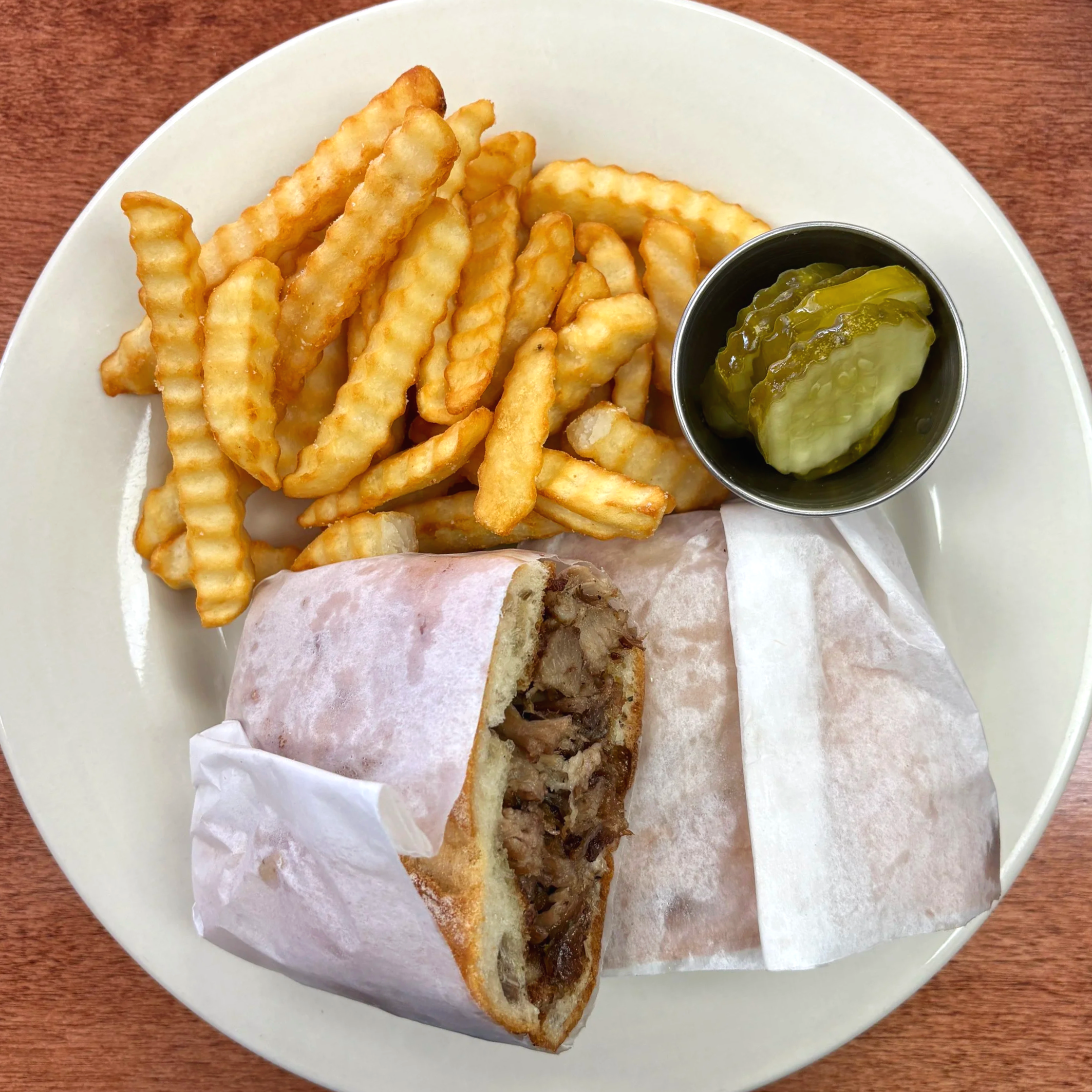 French fries, a pickle spear, and a meat-filled wrap on a white plate.