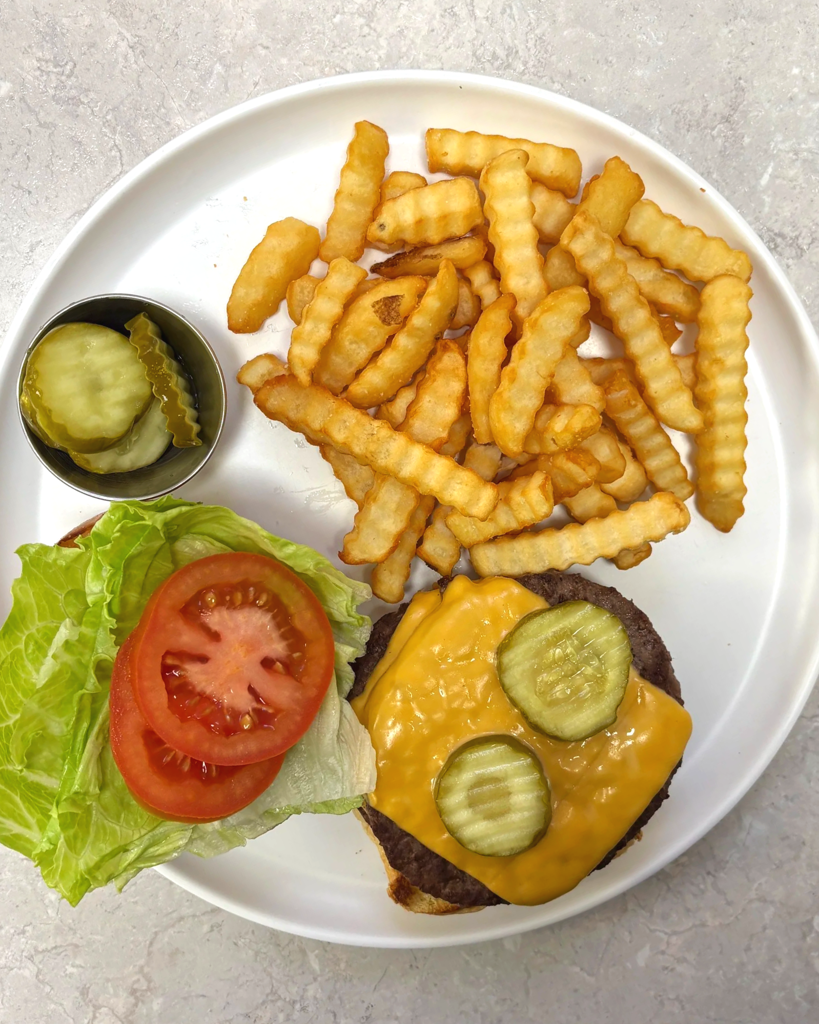 Plate with French fries, pickles, lettuce, tomato, cheeseburger with mustard and pickles.