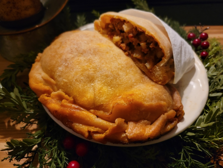 A baked meat pie with a golden crust, partially sliced to show a filling of meat and vegetables, on a white plate surrounded by holiday greenery and red berries.