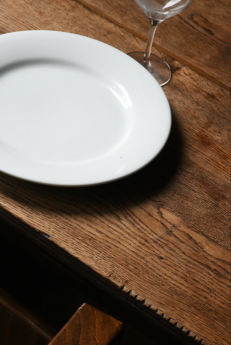 Une assiette blanche vide, un verre à vin vide, posés sur une table en bois.