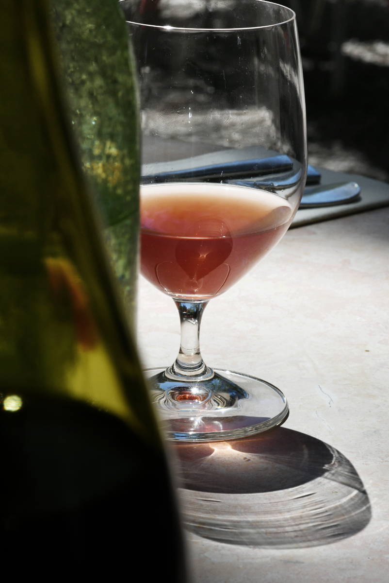 Verre de vin rosé sur une table en plein air, avec une bouteille verte partiellement visible à gauche.