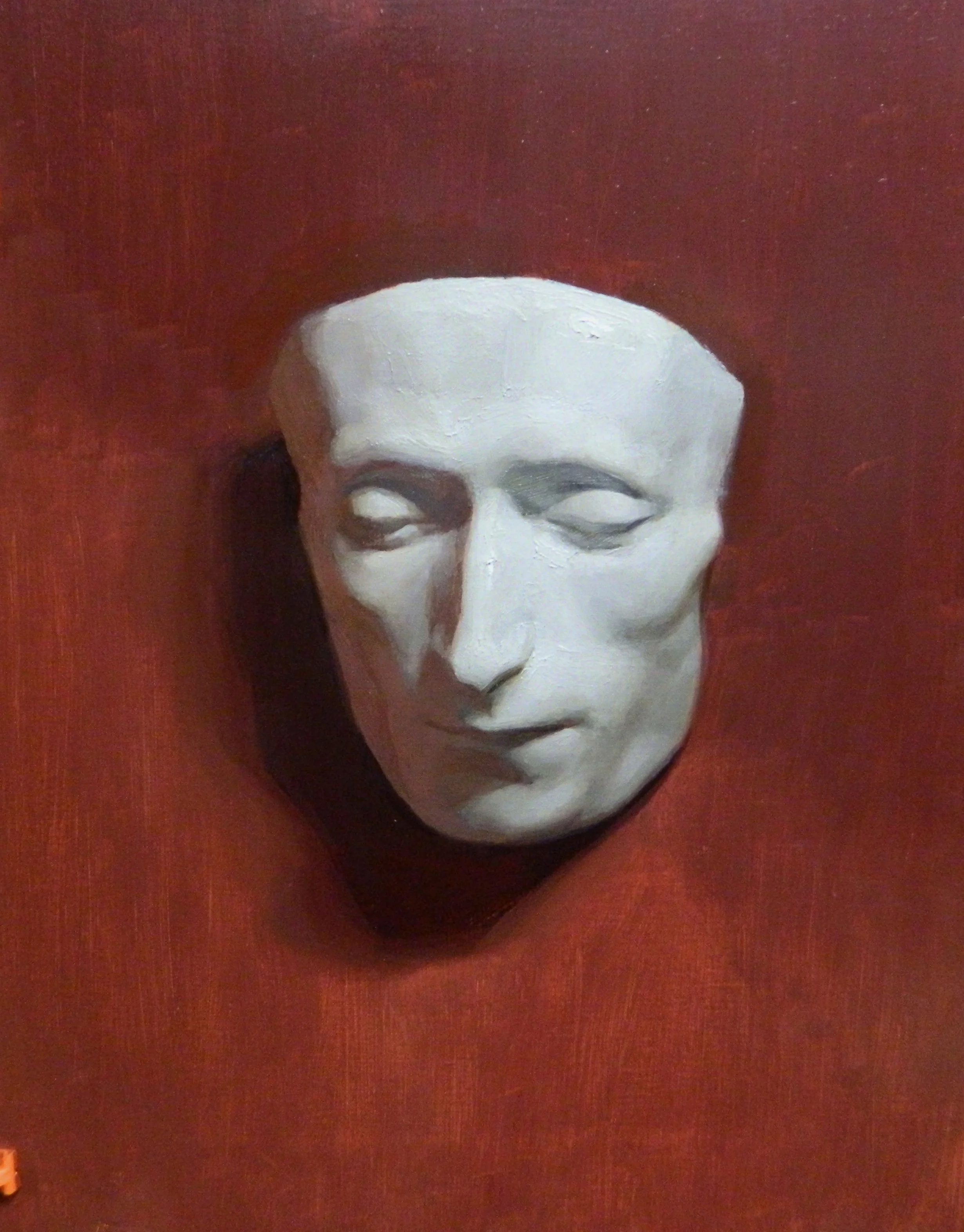 A white sculpted mask of a human face mounted on a dark red wall.