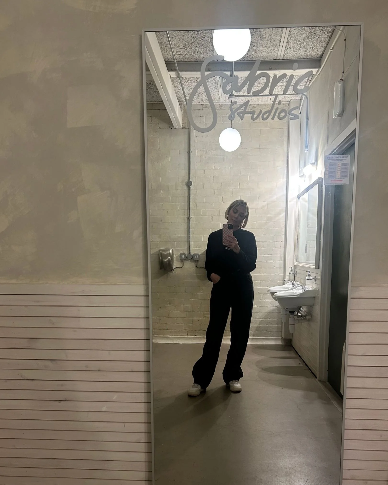 Melissa Woods, founder or Big ZigZag Studio is taking a selfie in a toilet mirror. She is wearing all black.