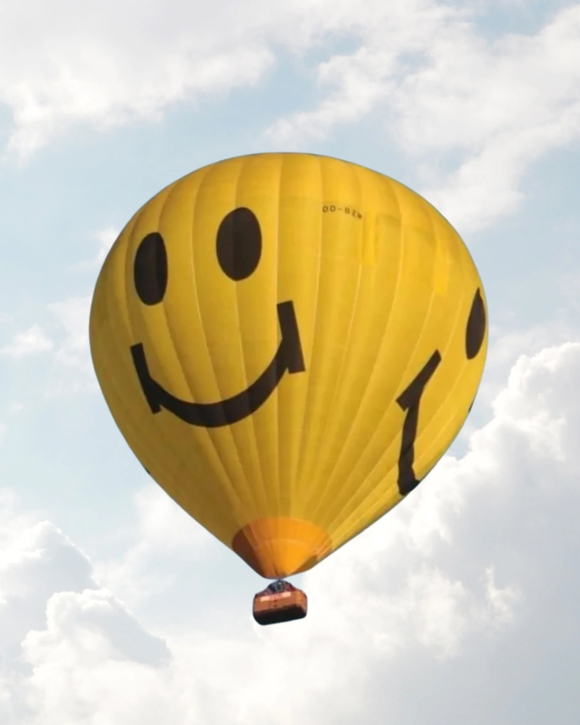 A yellow smiley face hot air balloon in the sky.