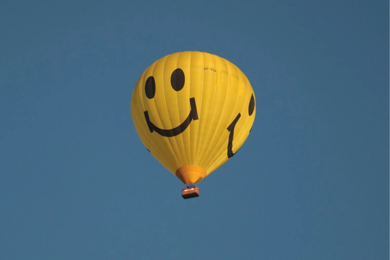 A yellow hot air balloon with a smiley face floating in the sky.