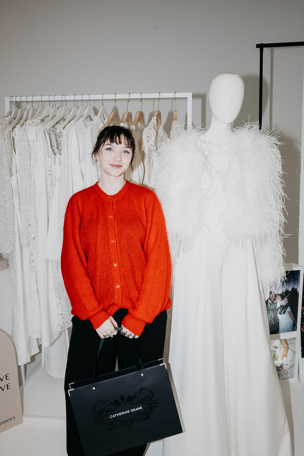 A woman in a red cardican is standing in front of a wedding dress at an event.