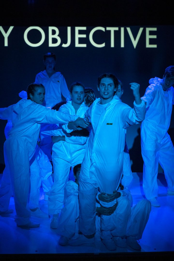 Photo from the production 'The Ark': a group of people in white coveralls perform under blue lighting.
