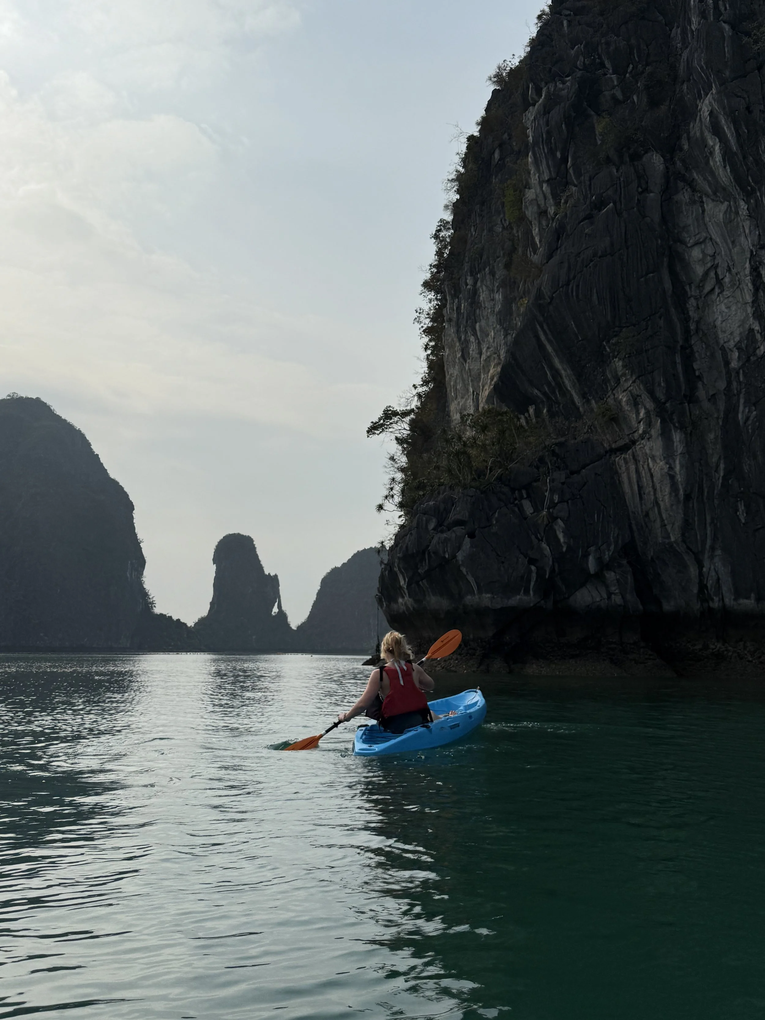 A person kayaking between large rocky cliffs in a body of water, with a distant rock formation in the background.