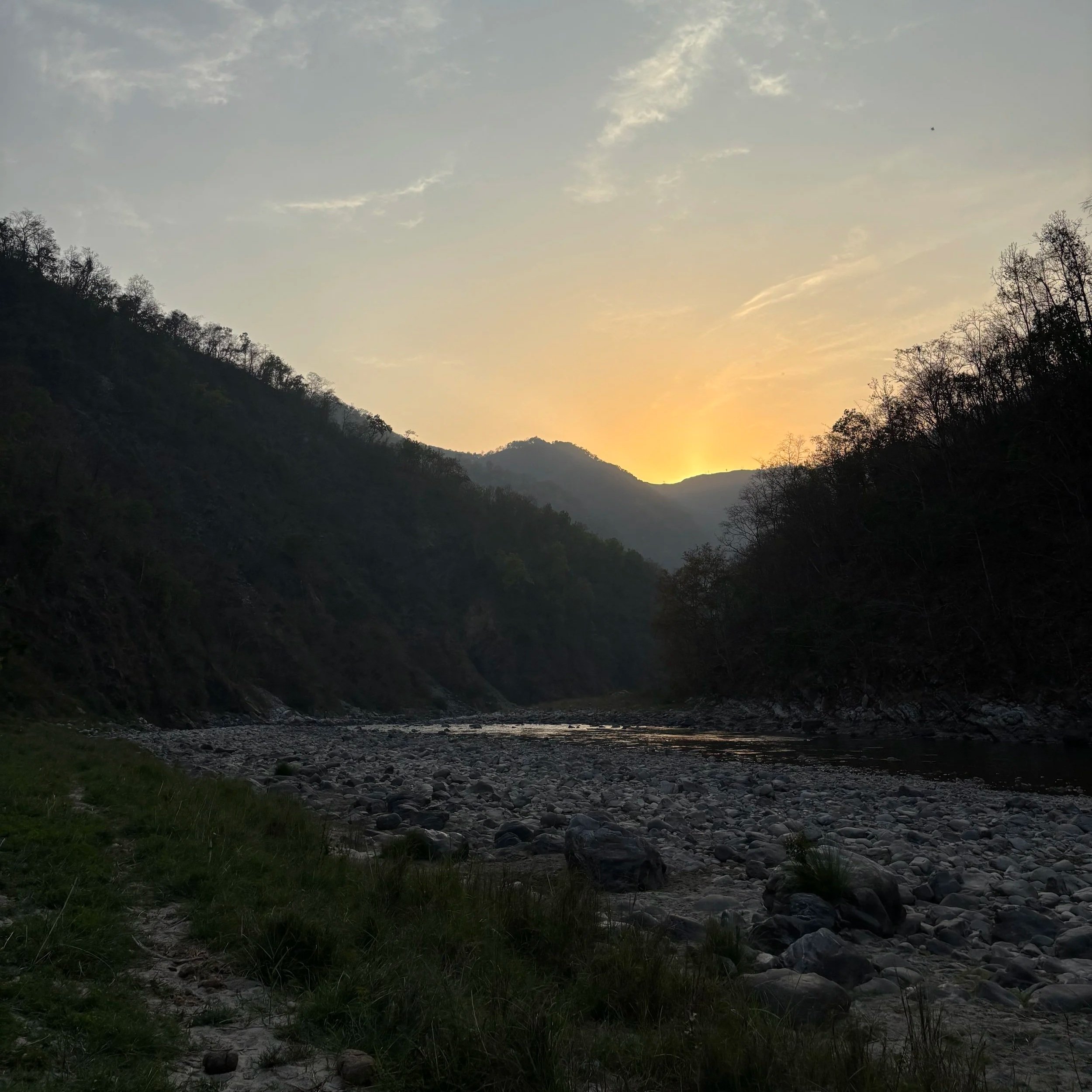 Sunset over a river valley with trees on the slopes of surrounding hills.