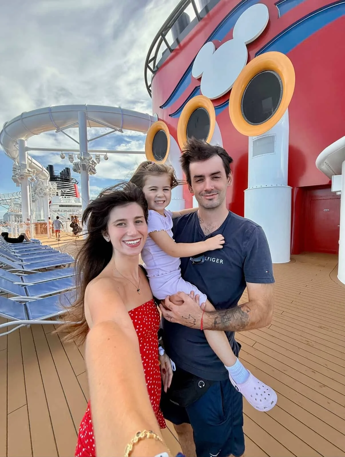 Chloe, James and their daughter posing together on a Disney cruise ship deck during a family travel experience