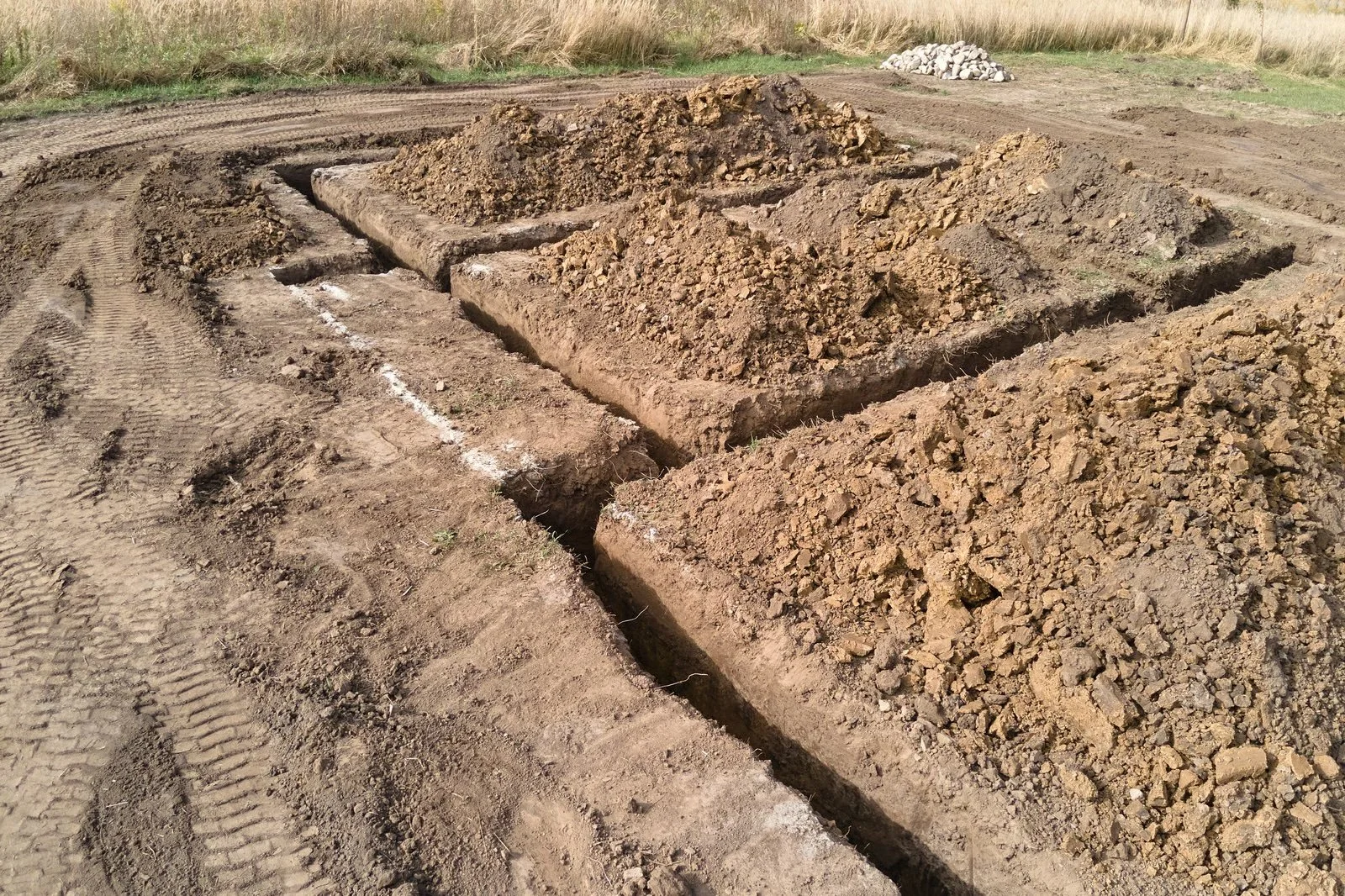 Construction site with trenches and piles of dirt, possibly for laying foundation or utilities.