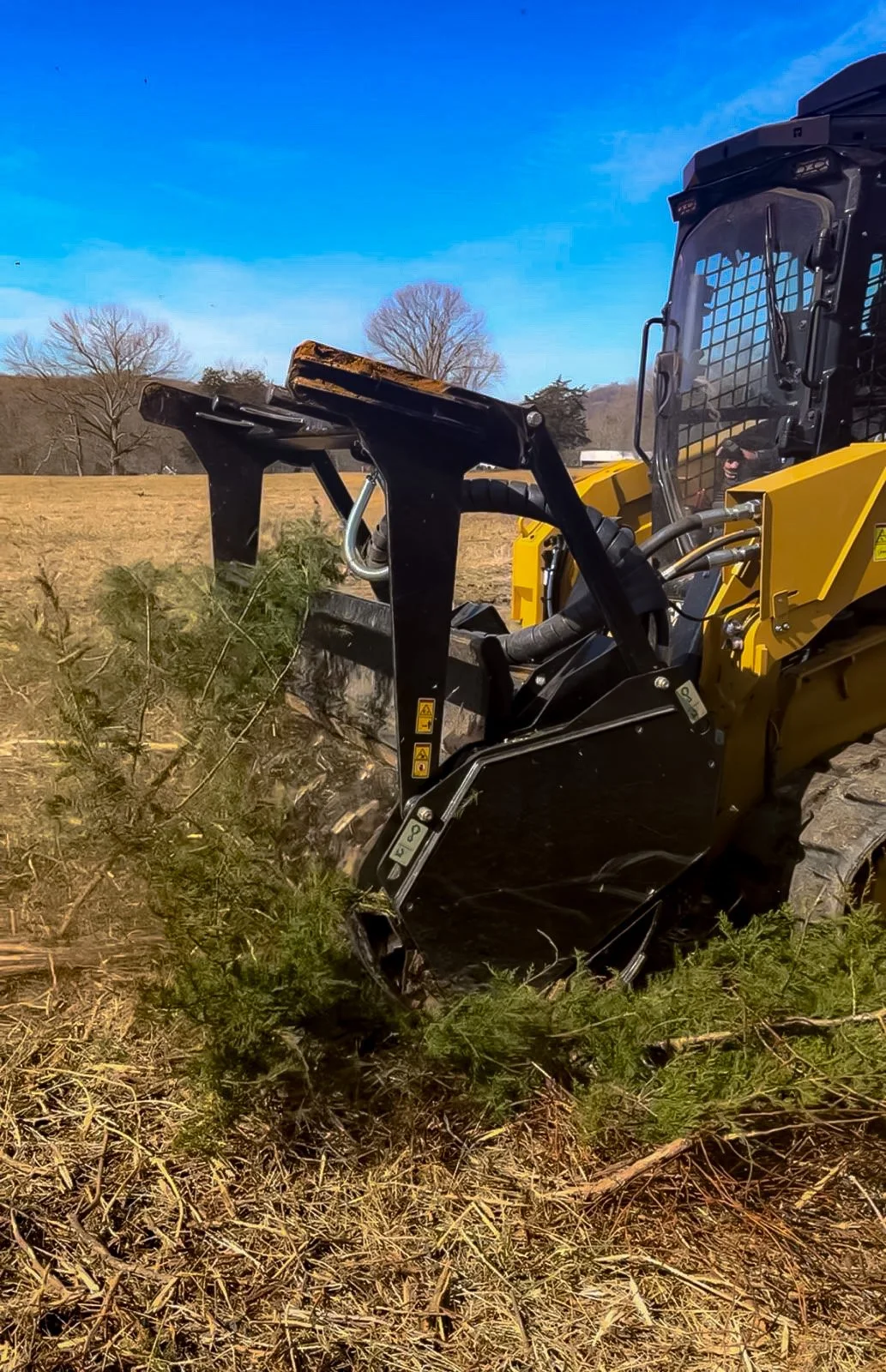 A yellow and black bulldozer pushing trees on a farm field.