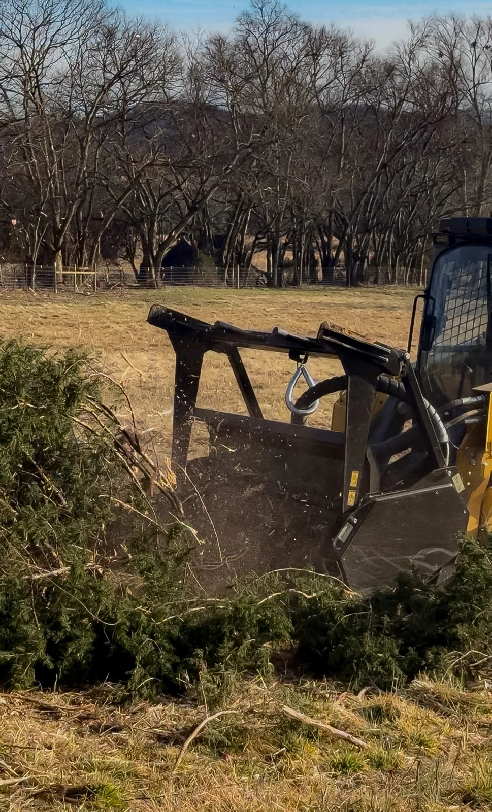A yellow bulldozer clearing a fallen tree in a field with leafless trees in the background on a clear day.