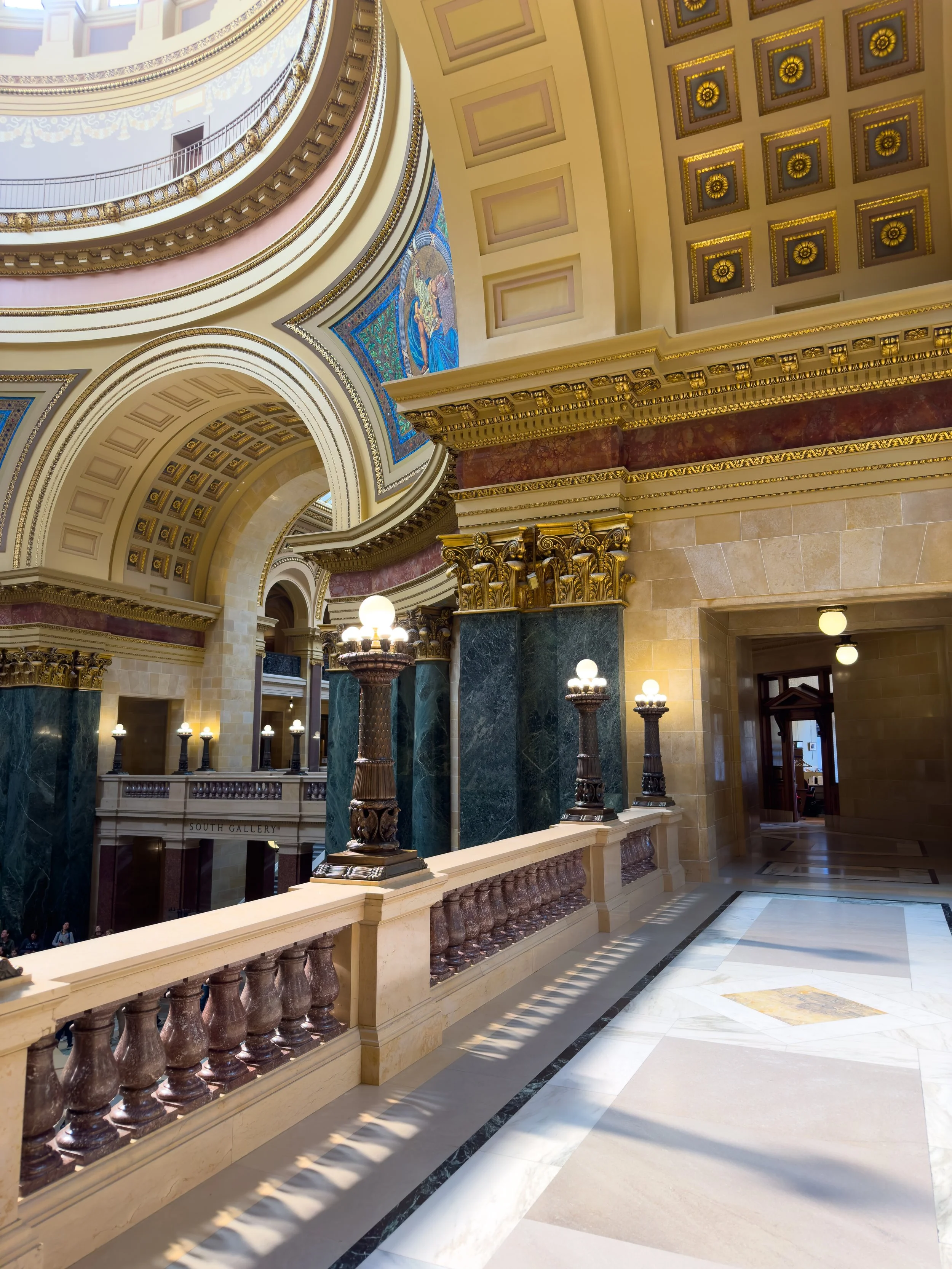 Interior view of the Wisconsin State Capitol Rotunda with ornate architecture, large arches, marble columns, and decorative gold accents.