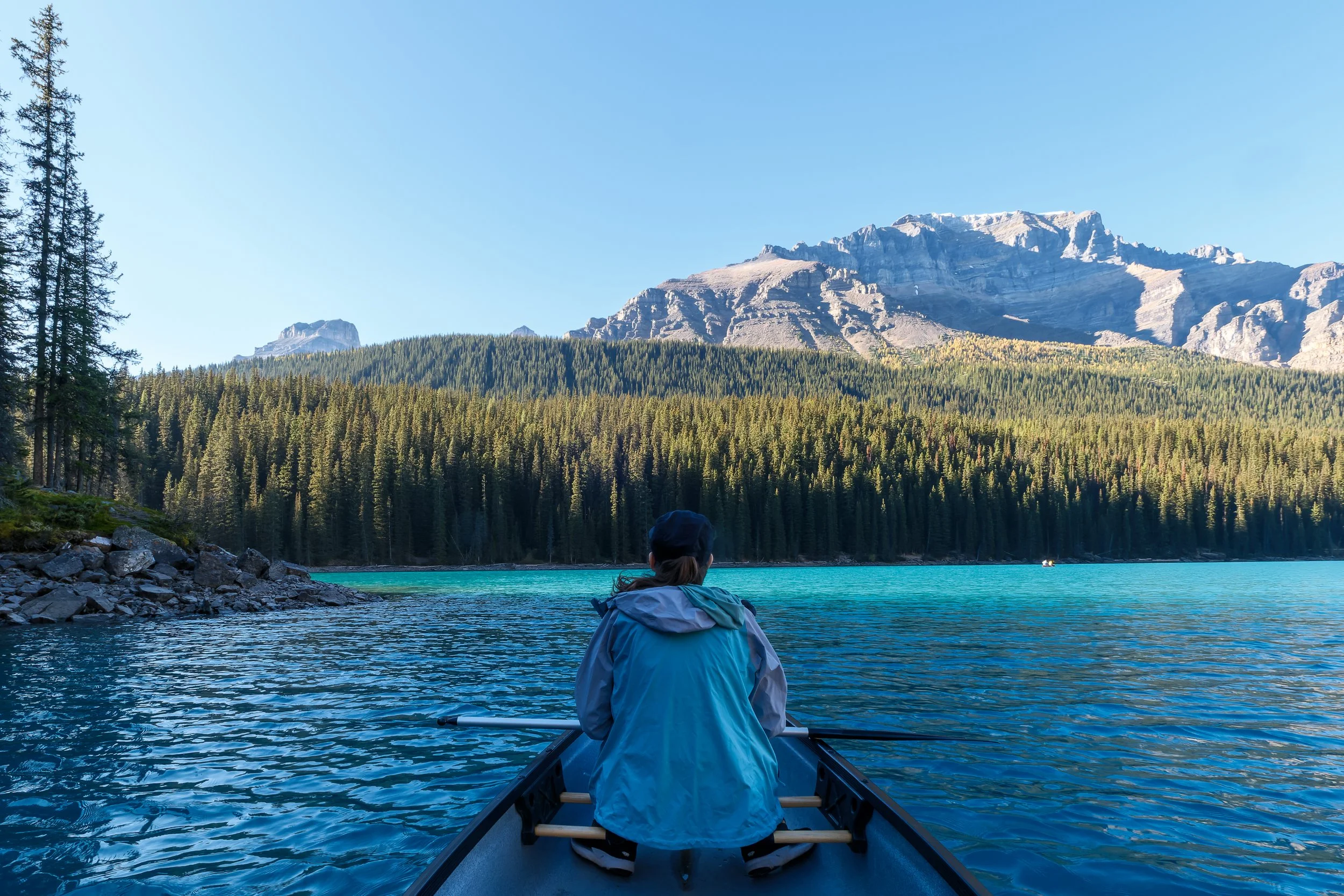 A person sitting in a canoe on Moraine Lake surrounded by forest and mountains in the background in Banff National Park.