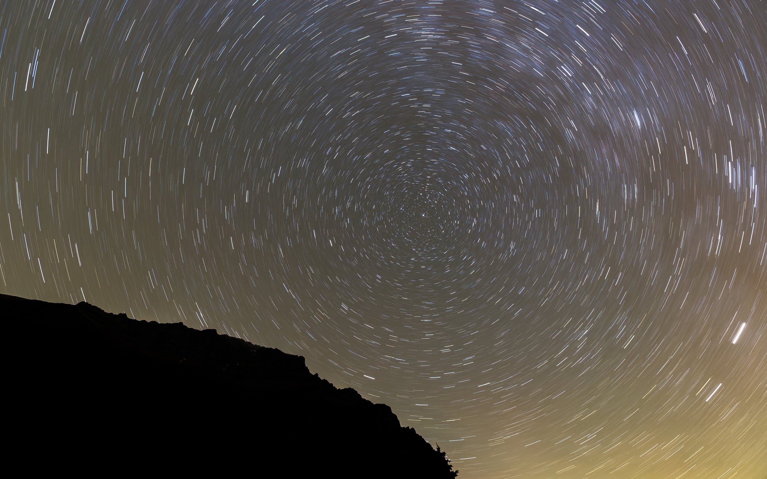 Long-exposure photo of star trails in the night sky over a silhouette of a mountain near Moraine Lake in Banff National Park.