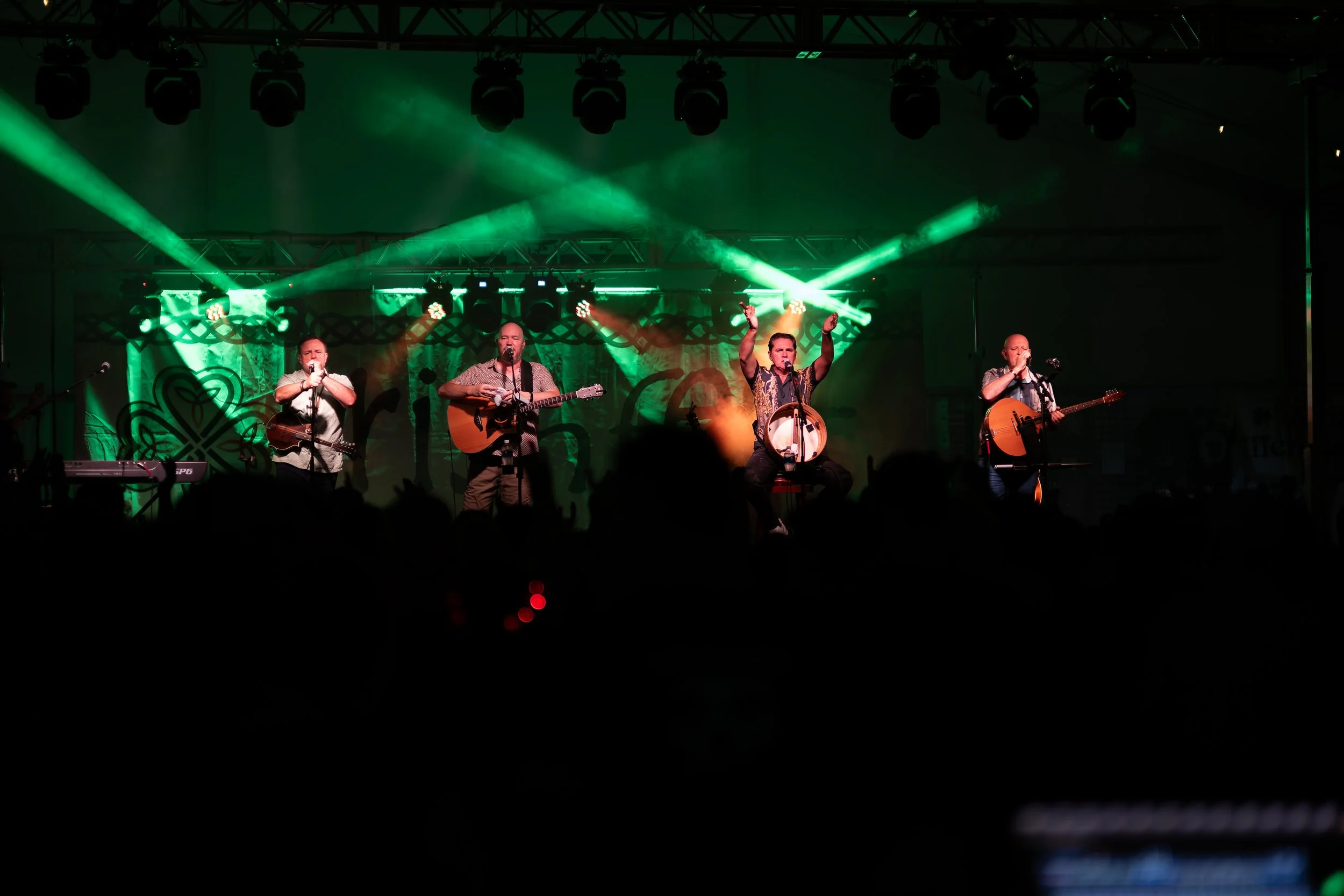 Musicians performing on stage with green stage lights and audience in foreground.
