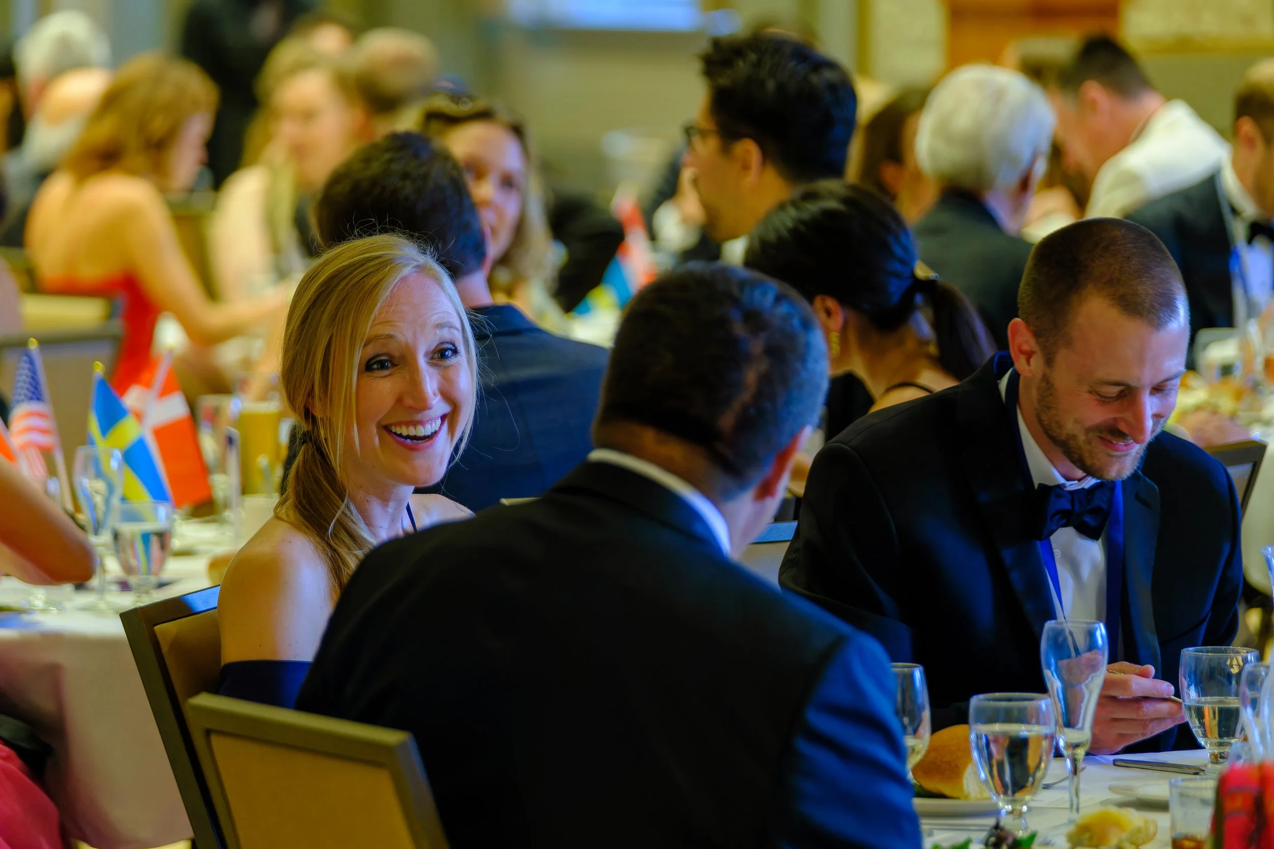 People dressed in formal attire attending a banquet, sitting at decorated tables with flags.