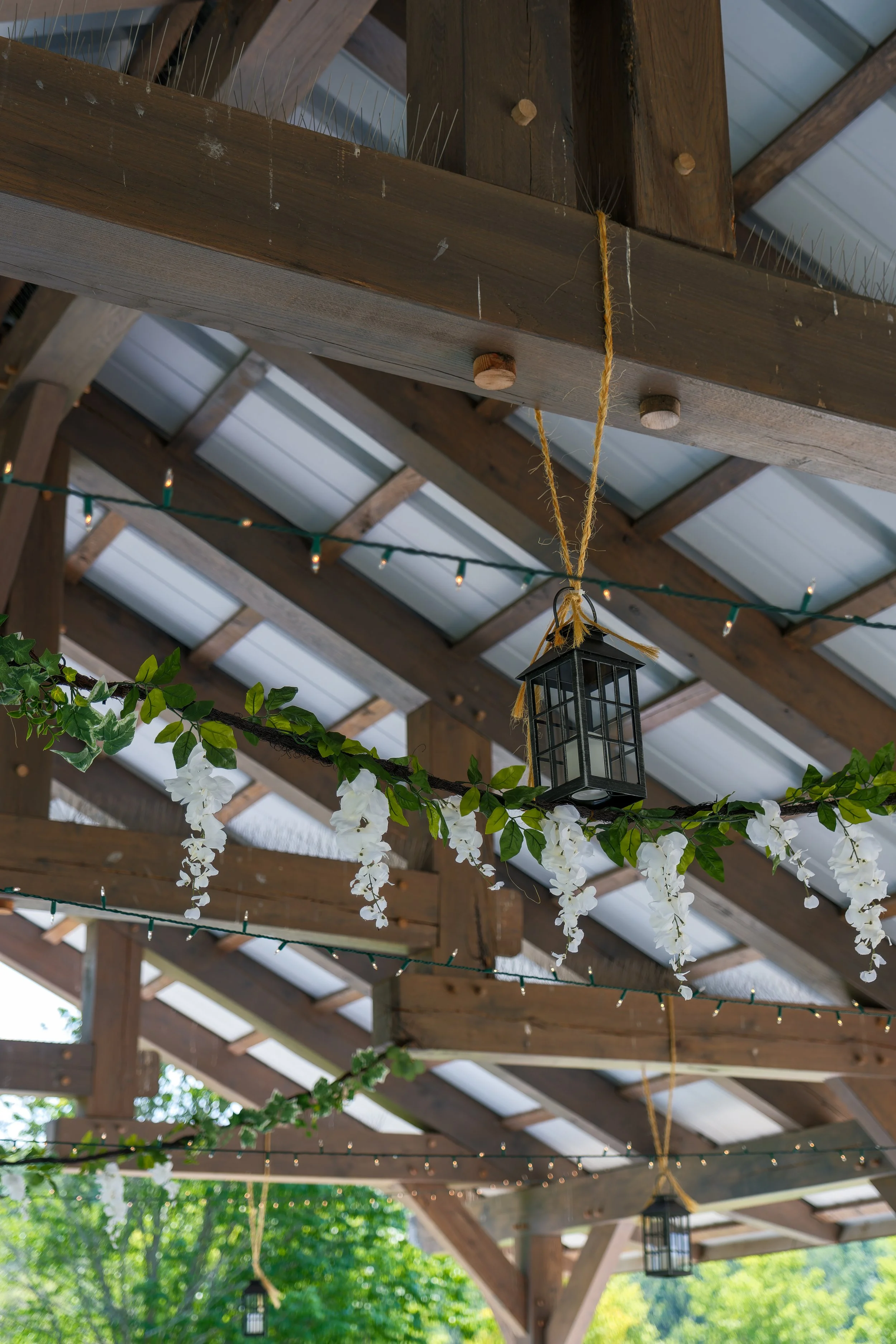 Decorative hanging lantern and string lights under a wooden roof structure with greenery outside.
