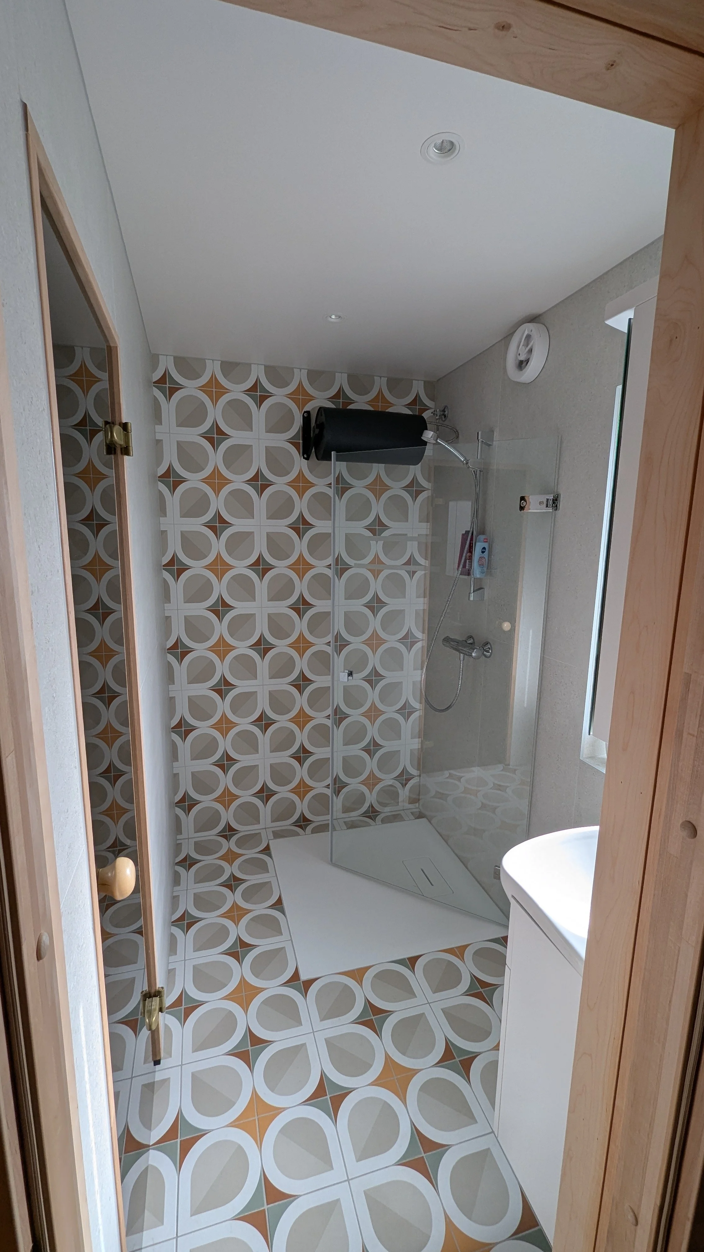 Bad med walk-in dusj, veggfliser med et geometrisk mønster i hvitt, beige og brunt, vask og speil