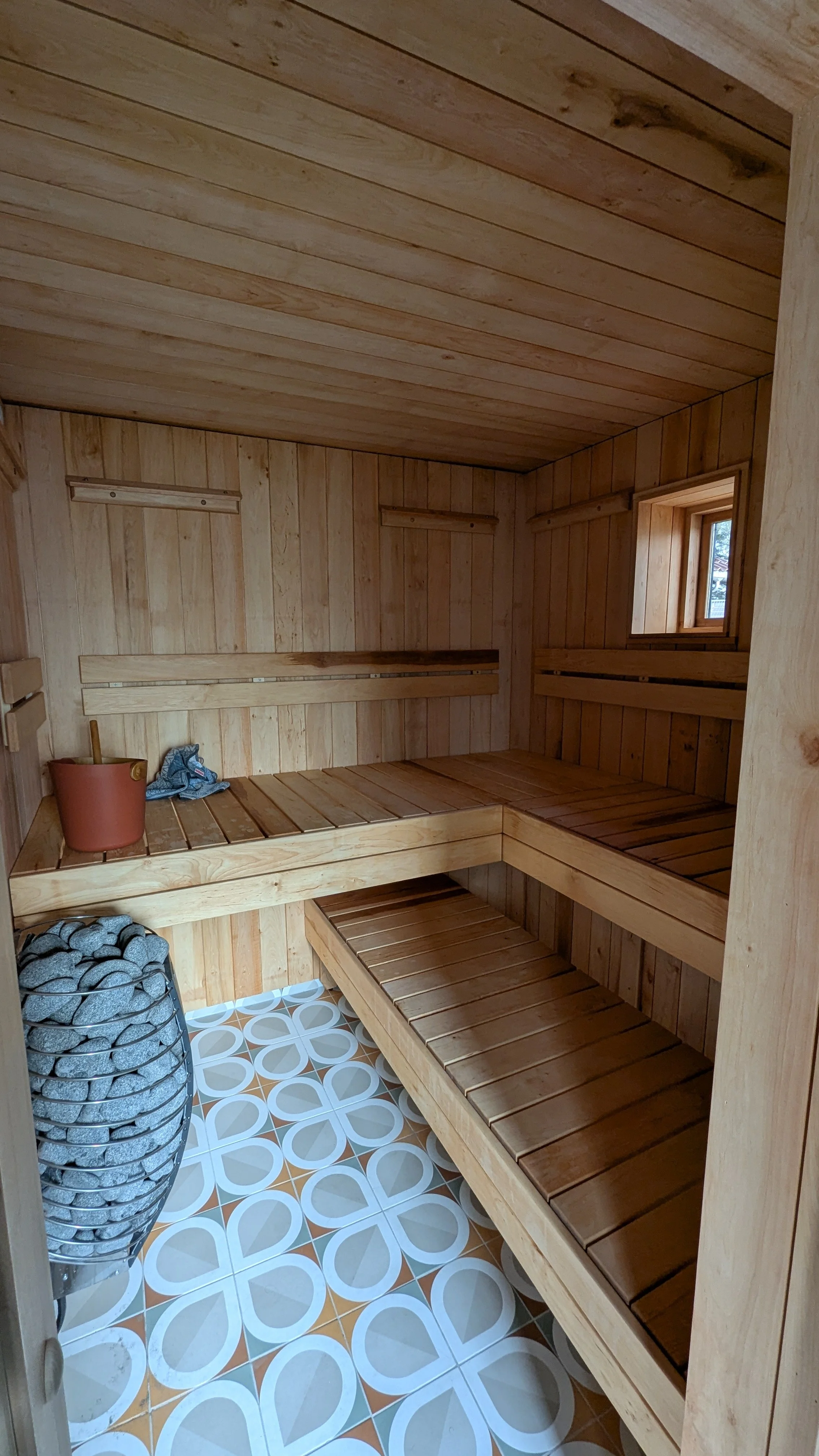 Innendørsmedisinsk badstue med trebenker, et badstueskaft, en varm steinovn, og et lite vindu.