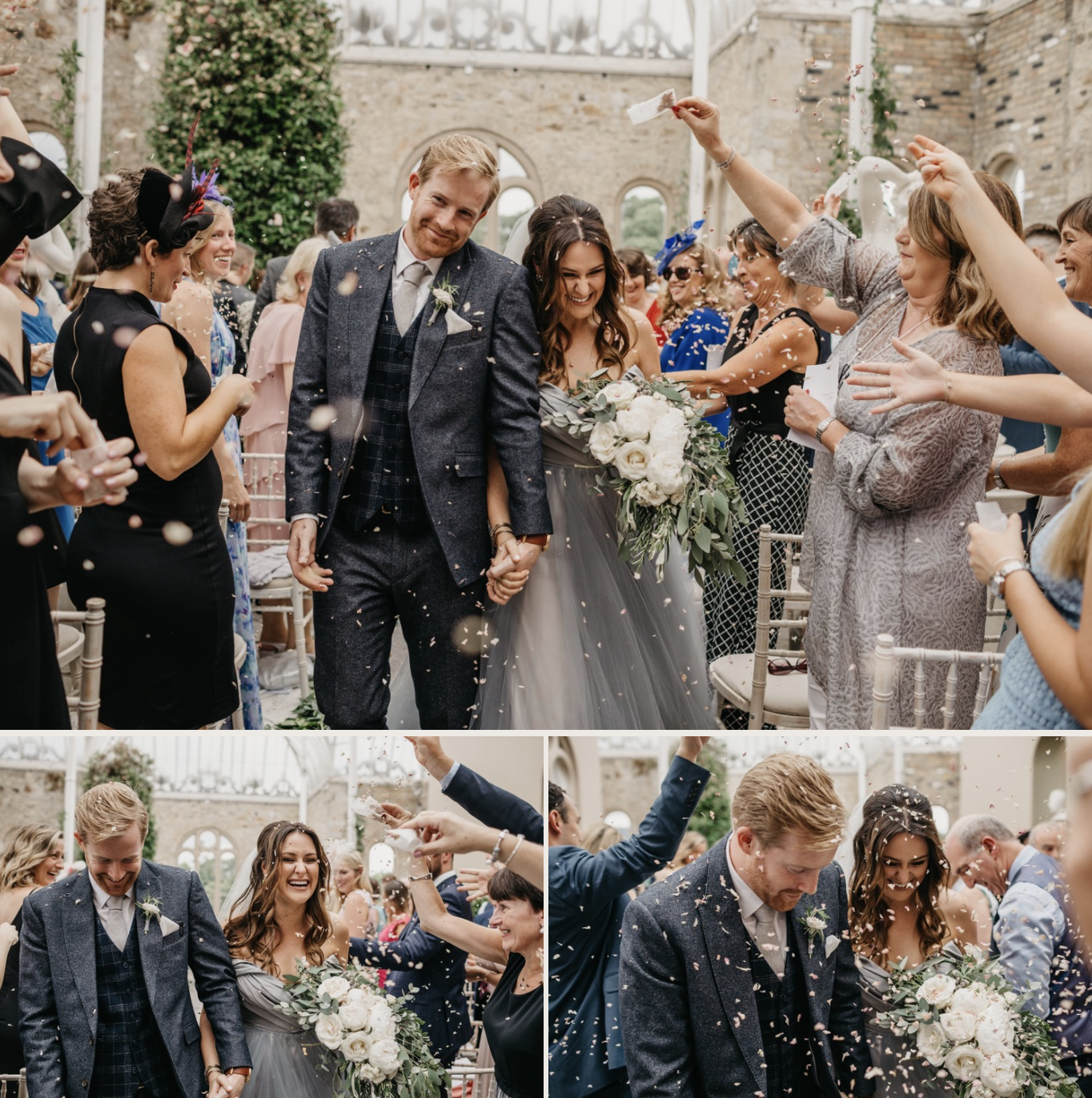 A newlywed couple walking hand in hand through a crowd at their wedding celebration, surrounded by guests throwing confetti and smiling. The bride holds a large bouquet of white flowers and greenery, and the groom is dressed in a dark suit. The setti
