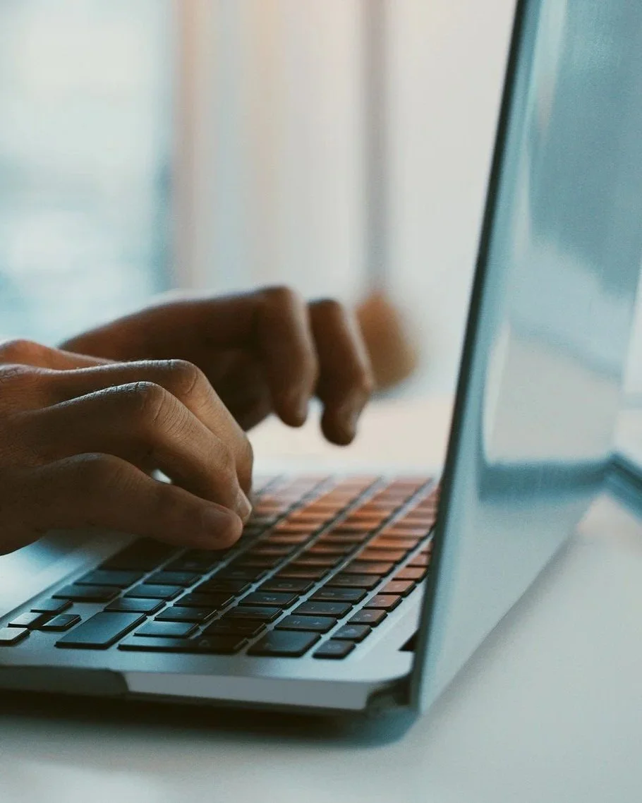 Main manipulant un clavier d'ordinateur portable avec un écran visible sur le côté droit.