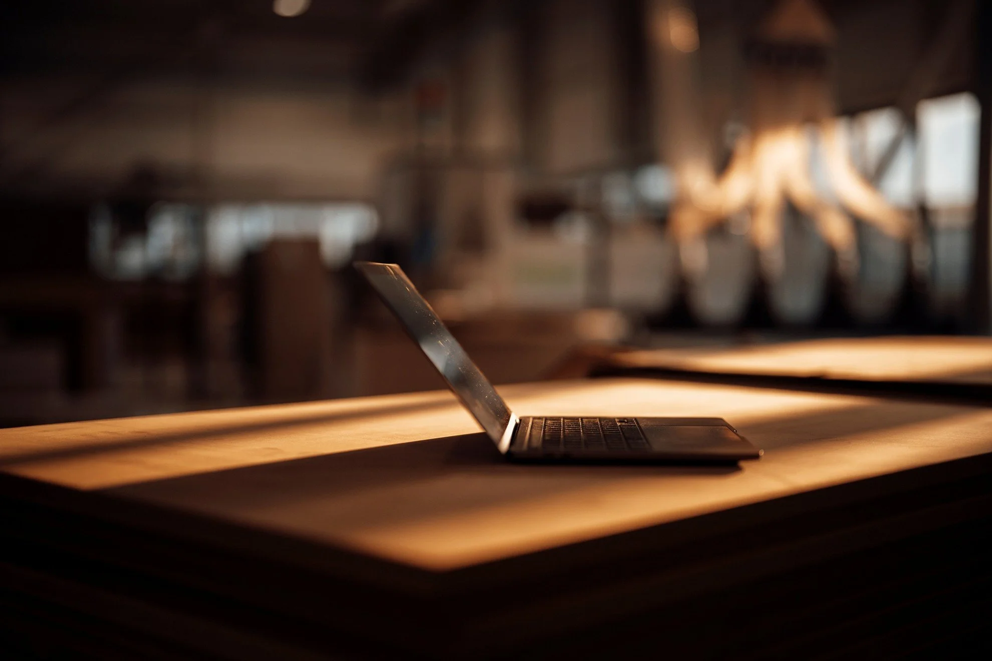 Un ordinateur portable ouvert sur une table en bois avec une lumière naturelle qui éclaire la scène, fond flou