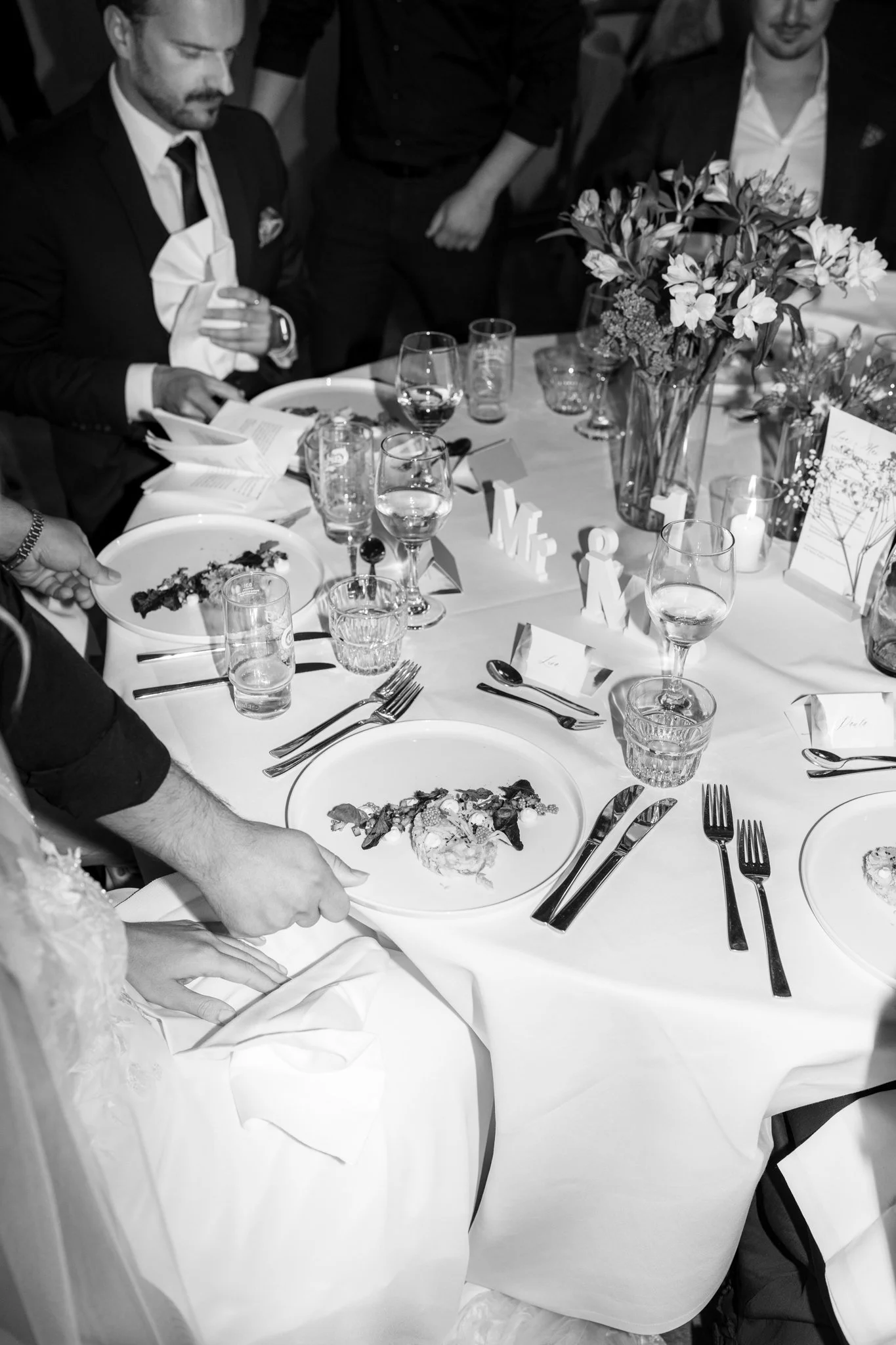 Eleganter Tisch bei einer Feier mit Blumen, Wein, Gläsern, Besteck und Tellern, auf denen Essen serviert wird.