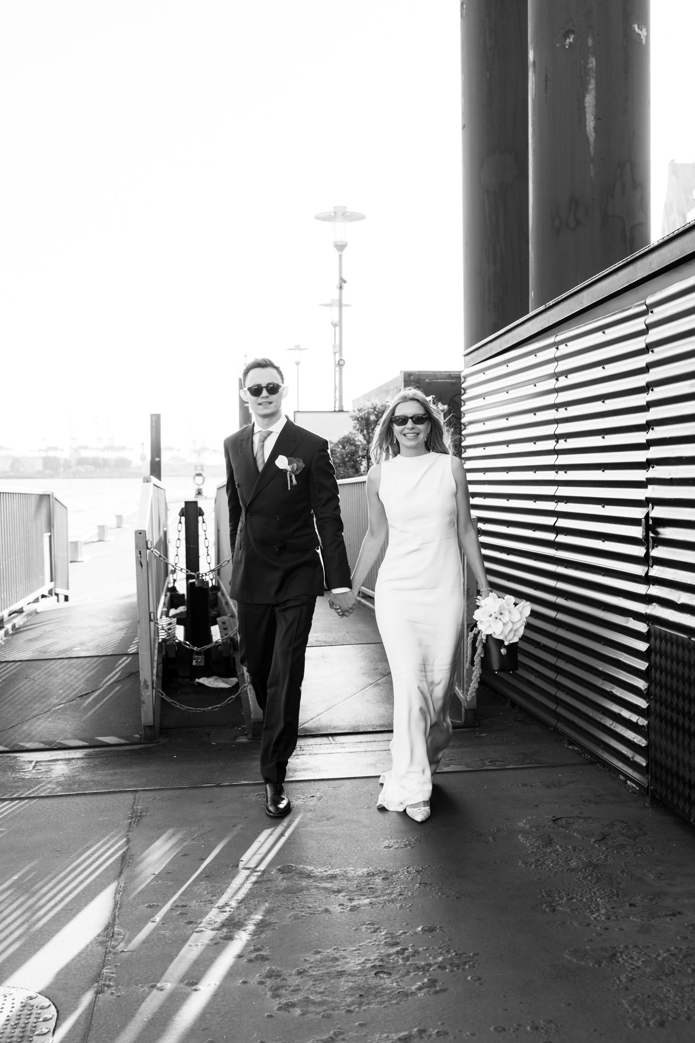 Ein schwarz-weiß Foto eines Paares in Hochzeitskleidung, das Hand in Hand läuft.