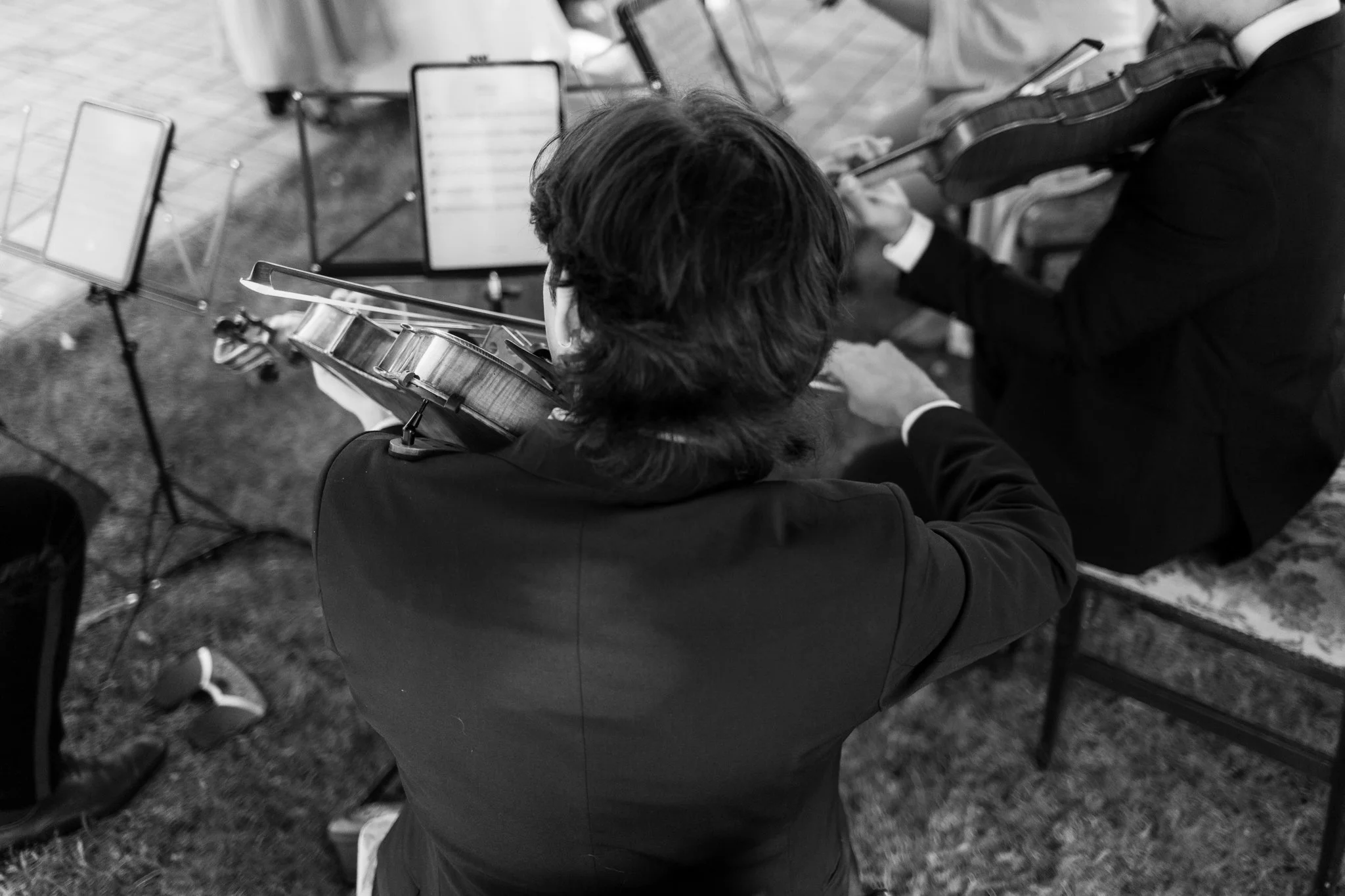 Zwei Musiker spielen Violine in einem Orchester, aufgenommen von oben, in Schwarz-Weiß.