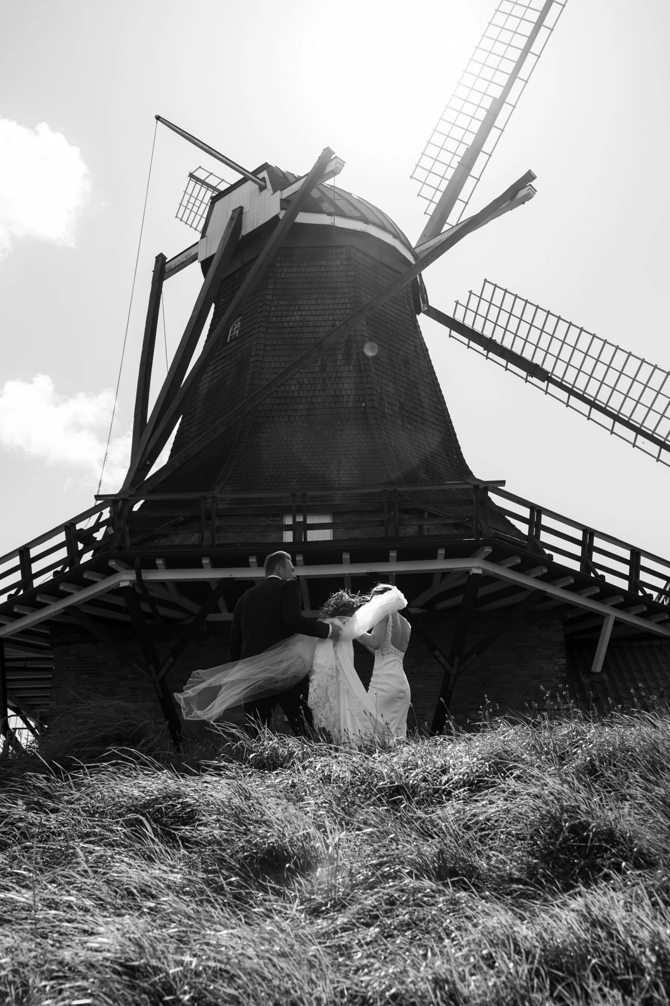 Ein Brautpaar vor einer historischen Windmühle, schwarz-weiß Fotografie.