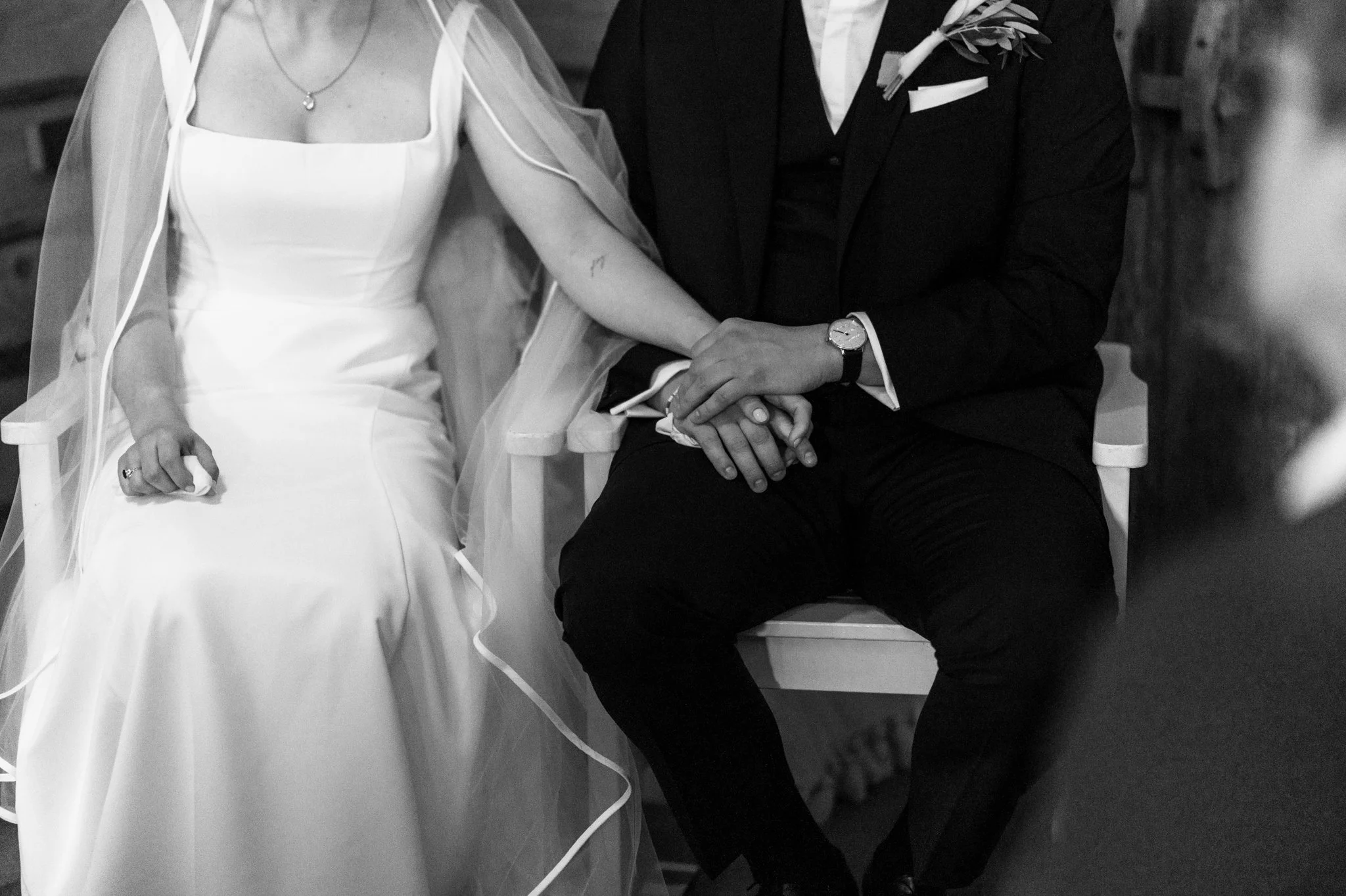 Eltern während ihrer Hochzeit, die Hand in Hand sitzen, im schwarzen und weißen Hochzeitsoutfit, in einer romantischen Atmosphäre.