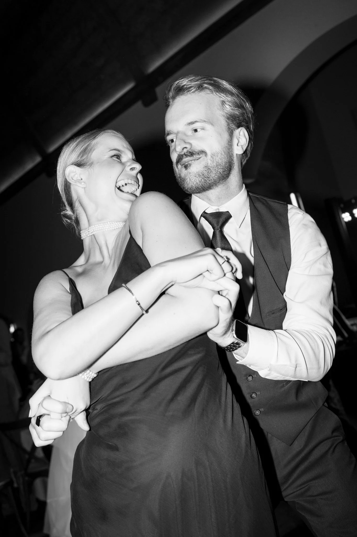 Ein schwarz-weiß Foto eines lachenden Paares, das beim Tanzen auf einer Feier zu sehen ist.