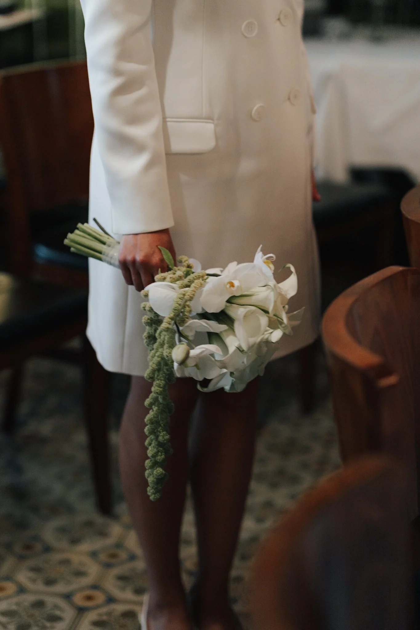 Eine Person in einem weißen Blazer hält einen Blumenstrauß aus weißen Calla-Lilien und anderen weißen Blumen in der Hand.