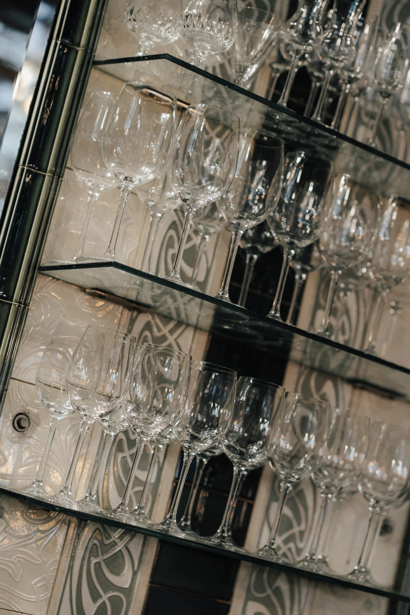 Mehrere leere Wein- und Sektgläser auf Glasregalen, mit bemaltem Hintergrund.