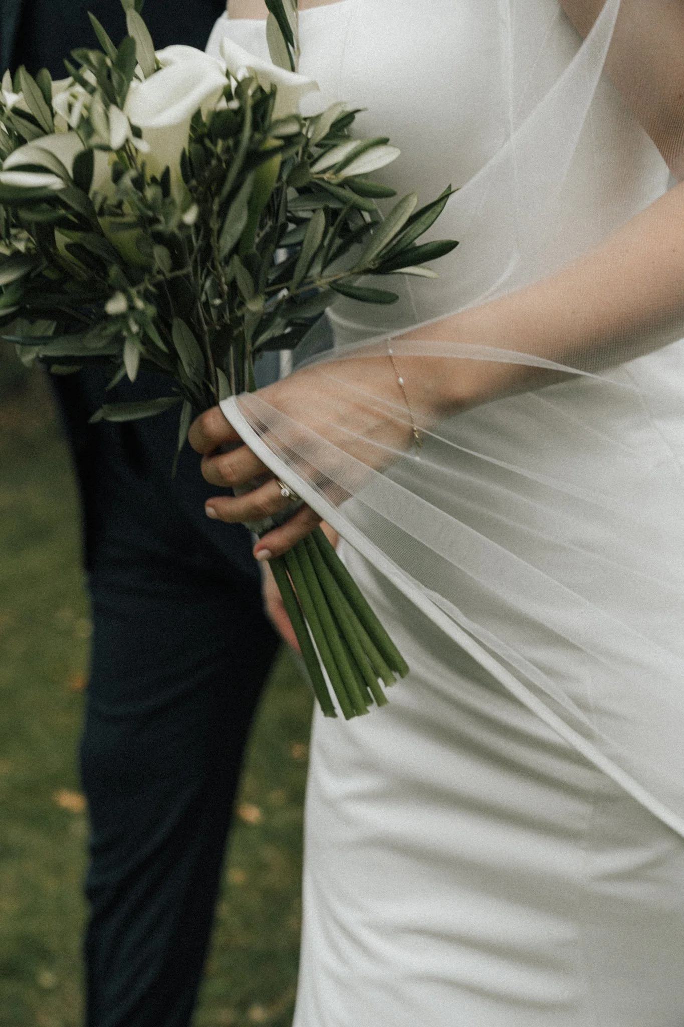 Eine Braut hält einen Blumenstrauß mit weißen Rosen und grünen Blättern in der Hand, während sie ein weißes Brautkleid trägt.