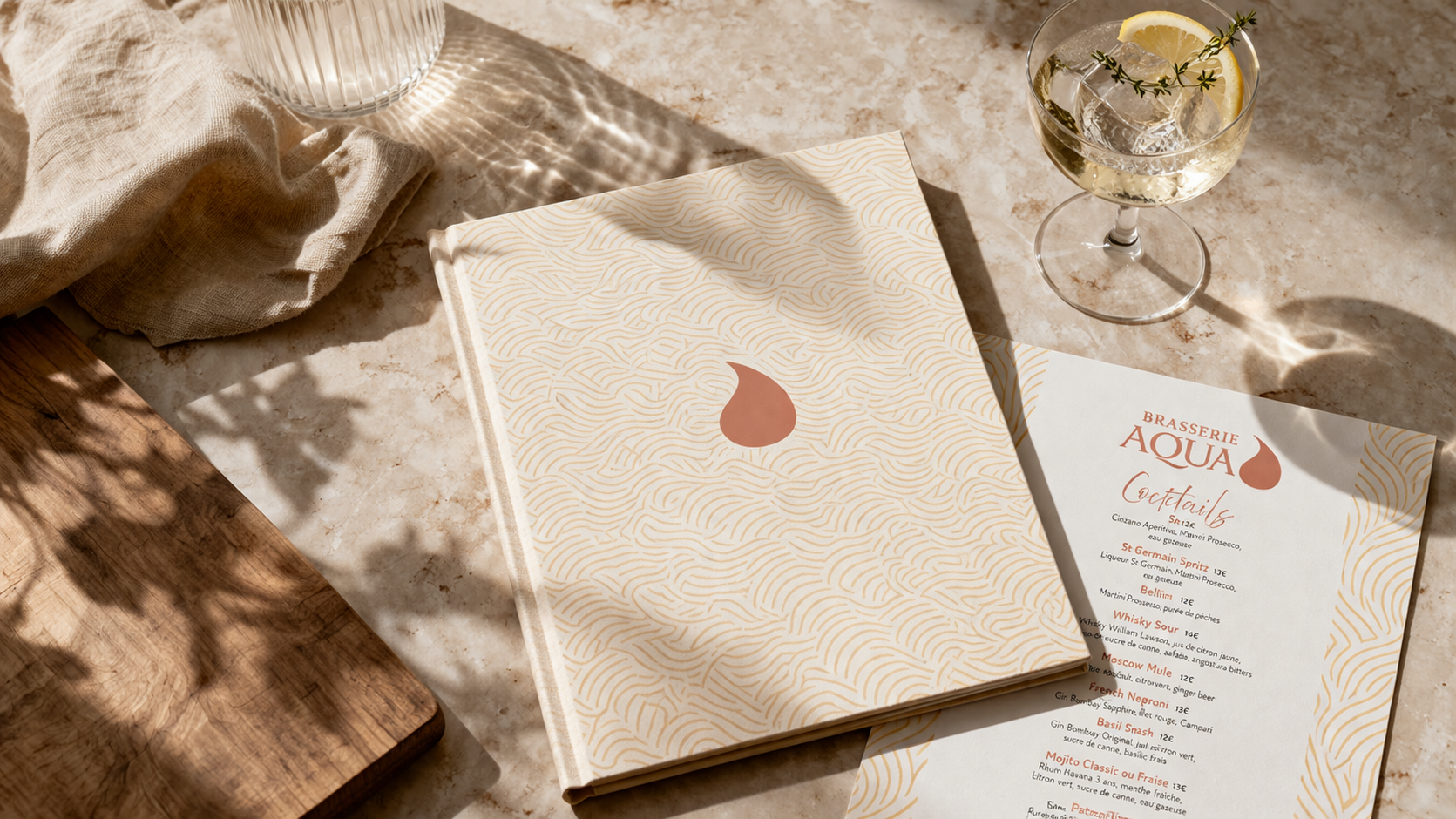Menu de la brasserie Aqua avec une liste de cocktails, une chanson en arrière-plan, un verre de cocktail citronné avec de la glace, et un chiffon beige sur une table en pierre.